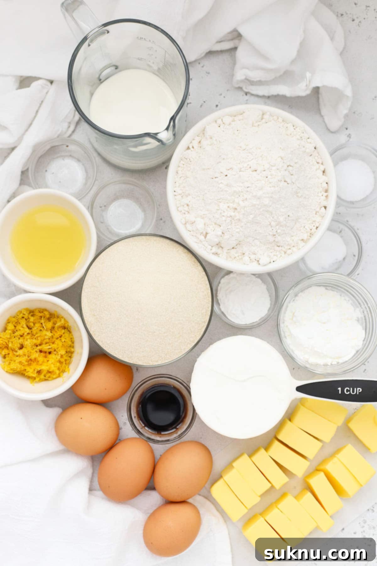 Zesty Gluten-Free Lemon Bundt Cake 3 Assorted ingredients for a gluten-free lemon bundt cake laid out on a white surface, including lemons, butter, sugar, and flour.