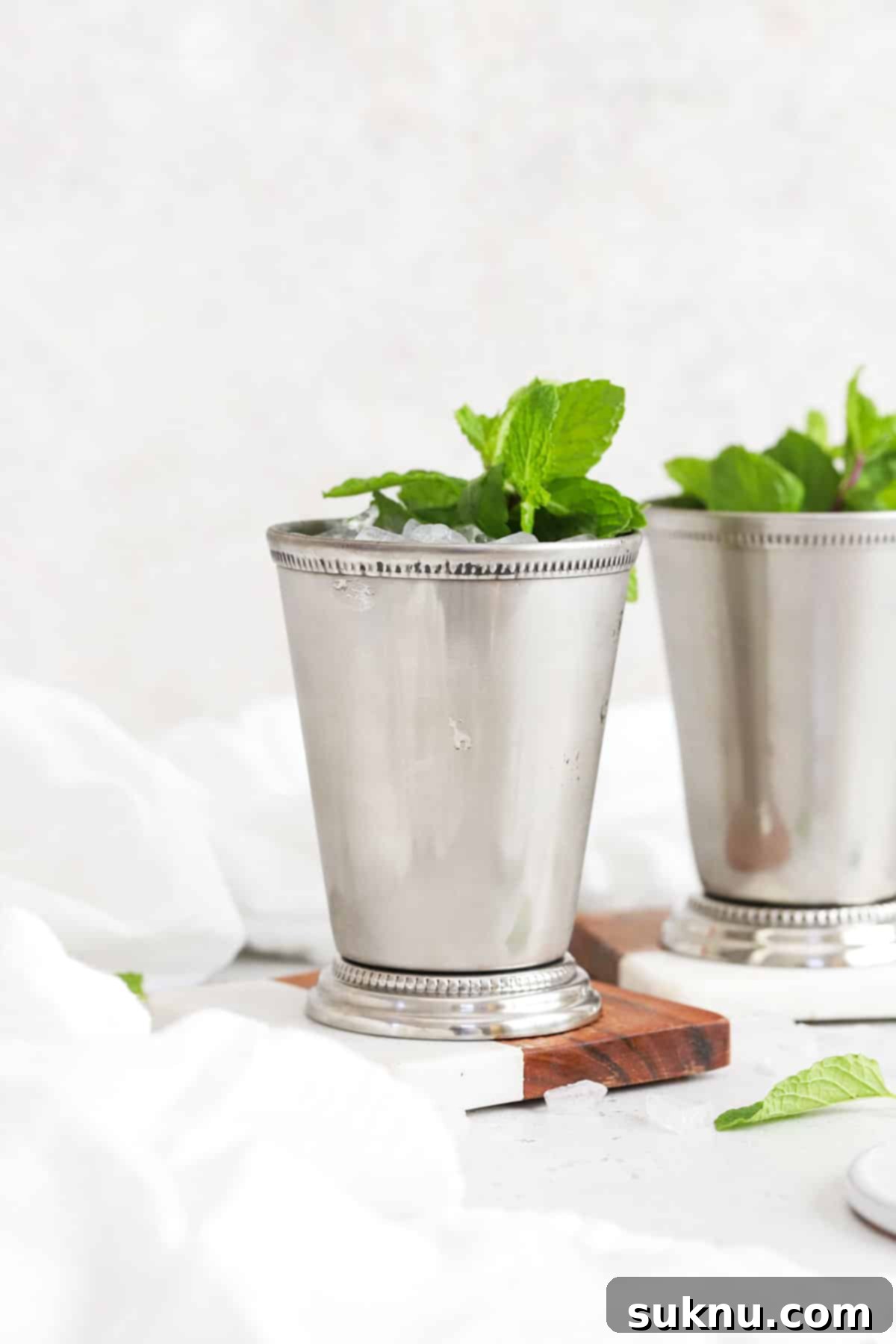 Disneyland Style Mint Julep 3 Two frosty virgin mint julep mocktails, presented beautifully in traditional metal julep cups. Garnish includes vibrant green mint sprigs, enhancing the refreshing appeal of the drinks. The background is softly blurred, keeping the focus on the inviting beverages.