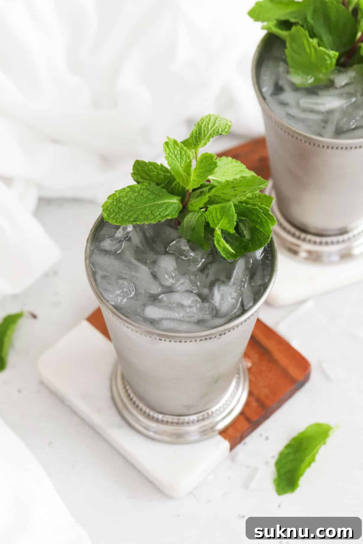 Disneyland Style Mint Julep 7 A vibrant close-up of two virgin mint julep mocktails in frosty metal cups, garnished with lush green mint sprigs and lemon slices. The ice is clearly visible, showing the refreshing, crushed texture. The focus is on the drinks, highlighting their crisp and inviting appearance.