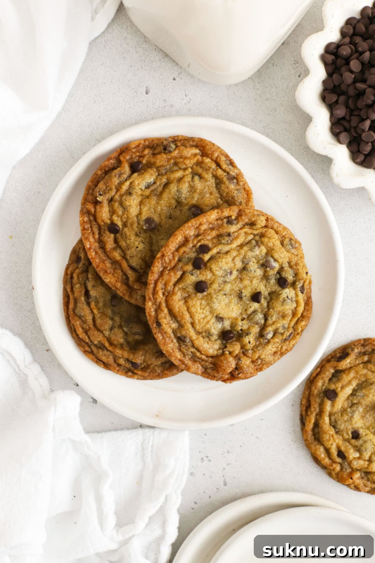 Ultimate Thin and Crispy Gluten-Free Chocolate Chip Cookies 2 Three crisp gluten-free chocolate chip cookies on a white plate, showcasing their golden brown tops and delicate edges