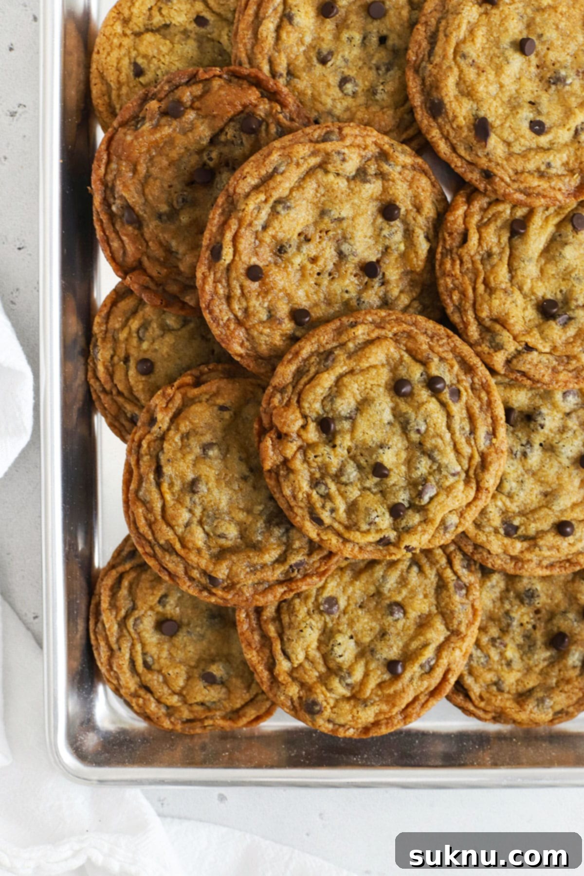 Ultimate Thin and Crispy Gluten-Free Chocolate Chip Cookies 3 thin, crispy gluten free chocolate chip cookies stacked on a cookie sheet, perfectly golden