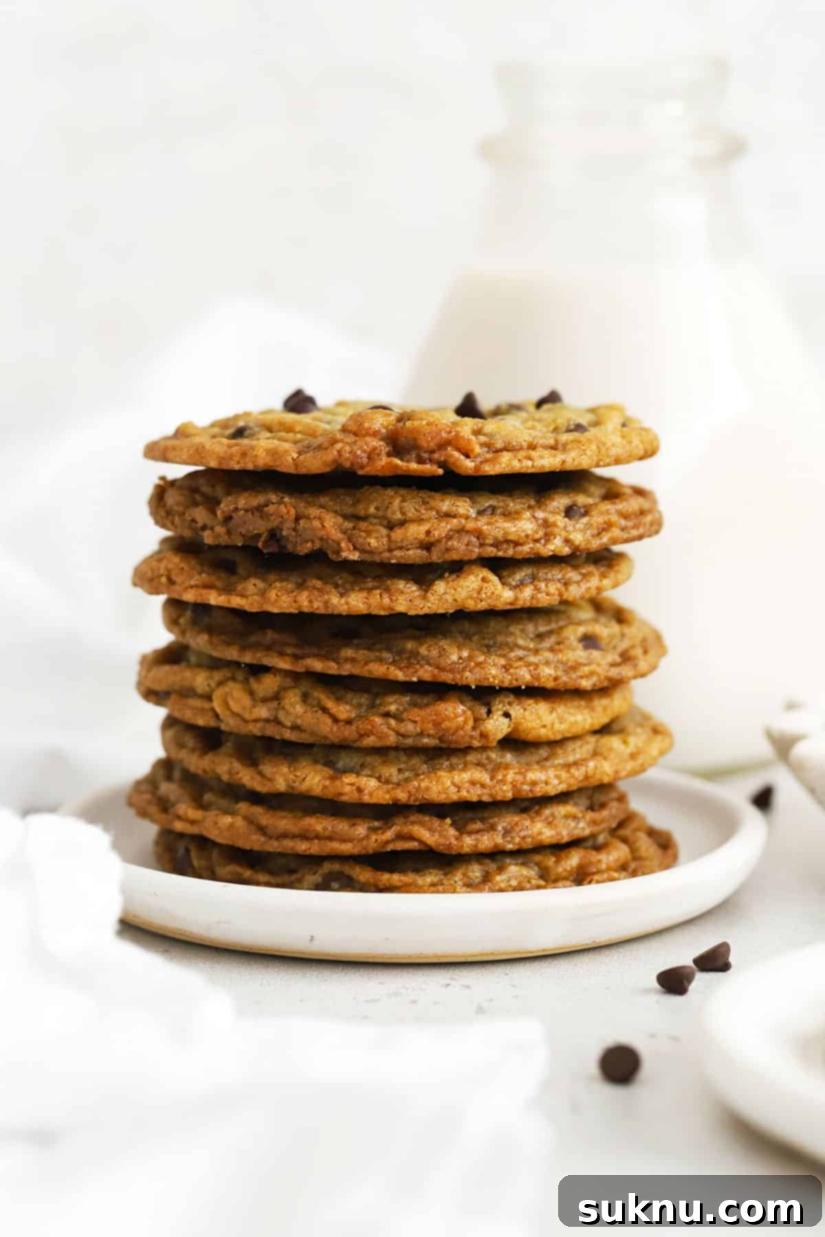 Ultimate Thin and Crispy Gluten-Free Chocolate Chip Cookies 6 A stack of thin, crispy gluten-free chocolate chip cookies next to a jar of milk in the background