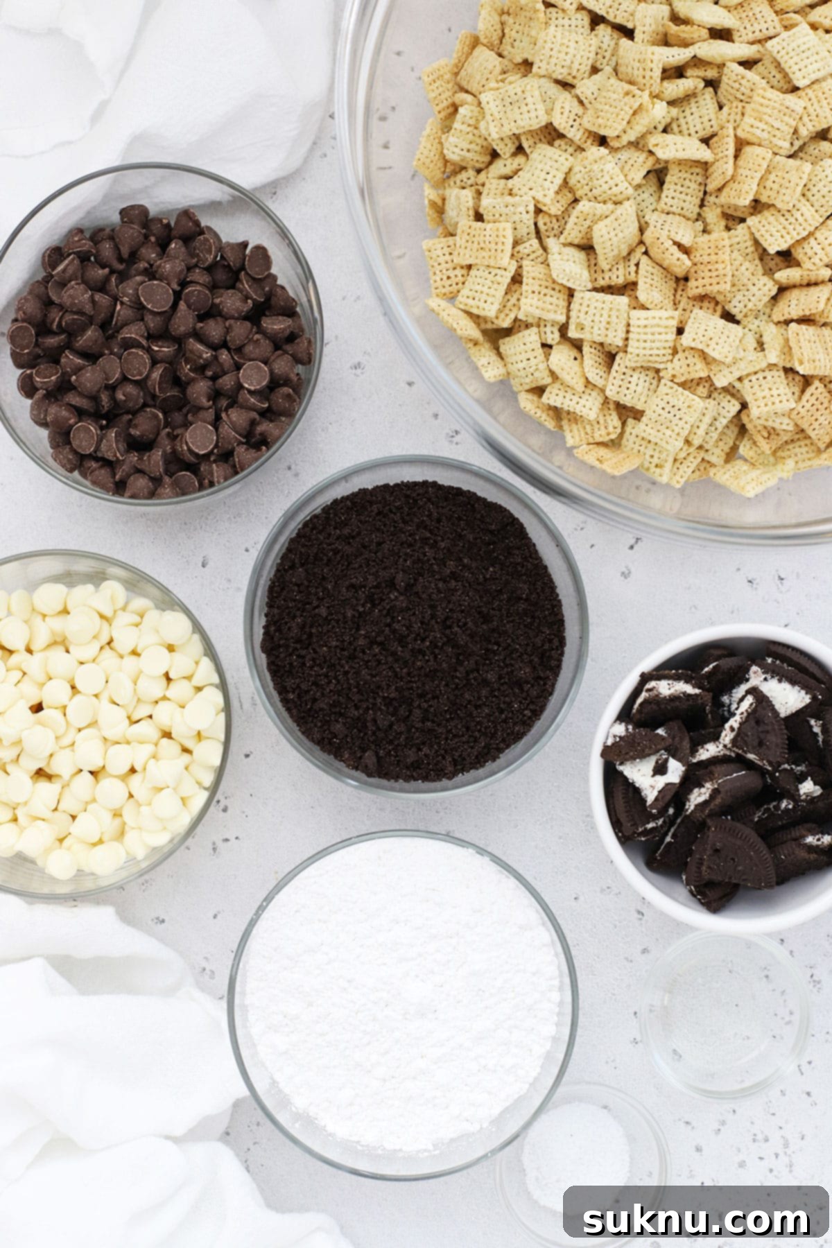 A flat lay showing the simple ingredients needed for making cookies and cream muddy buddies, including Chex cereal, gluten-free Oreos, chocolate chips, and powdered sugar.