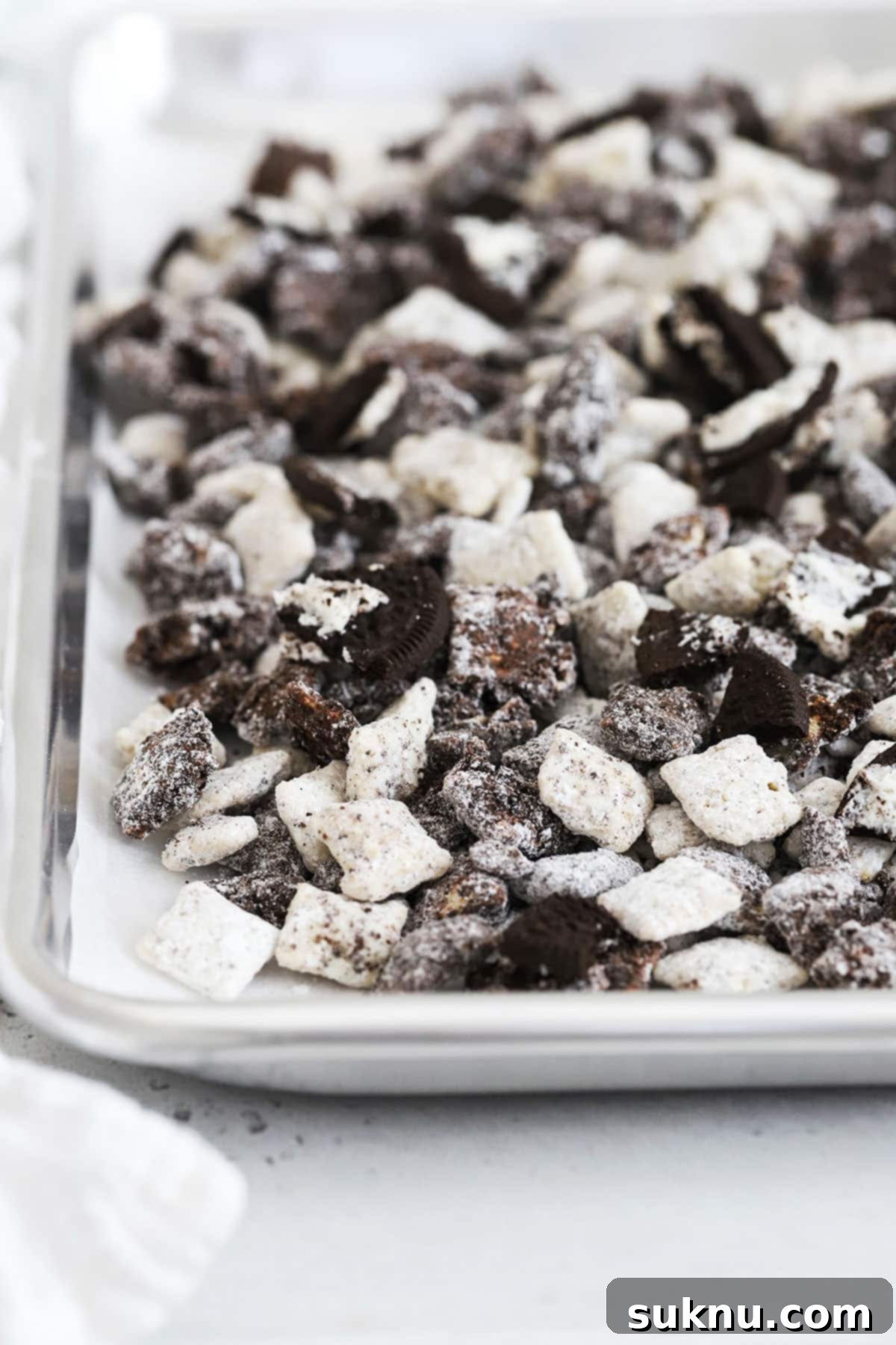 A baking sheet laden with a generous batch of finished oreo muddy buddies, featuring the contrasting black and white pieces and scattered chopped Oreos.