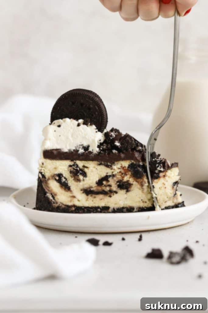A fork cutting into a decadent slice of gluten-free Oreo cheesecake on a white plate, revealing creamy layers and cookie crust.