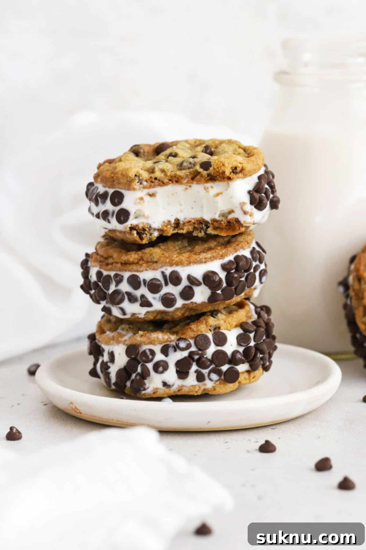 Gluten-free cookie ice cream sandwiches stacked on a white plate, showcasing thin, crisp chocolate chip cookies and creamy vanilla ice cream.