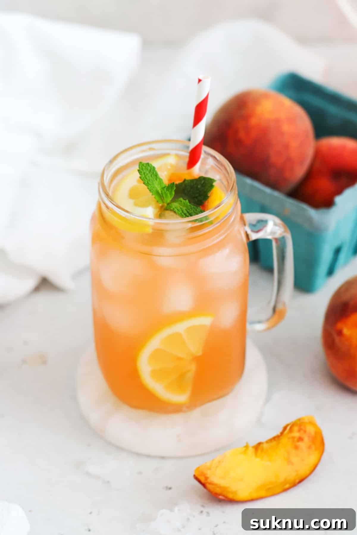 Two mason jar glasses filled with homemade peach lemonade, garnished with fresh peach slices and mint sprigs.