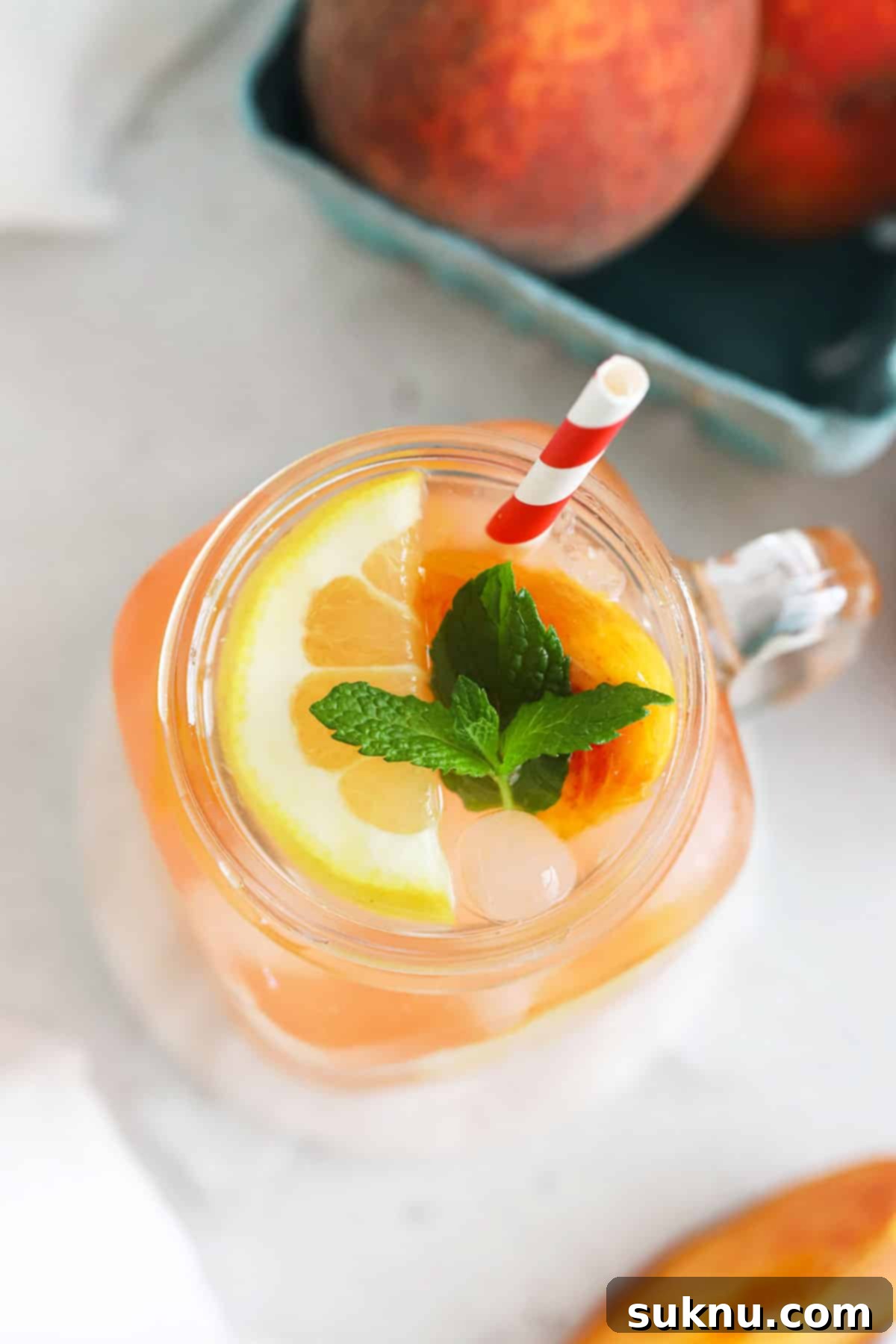 Three mason jar glasses filled with homemade peach lemonade, each adorned with a different garnish: peach slices, mint, and lemon wheels.
