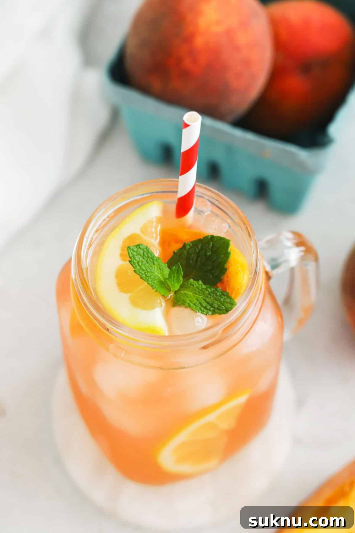 A close-up of a mason jar glass filled with homemade peach lemonade, showing the beautiful peachy-pink color and condensation, suggesting a cold, refreshing drink.