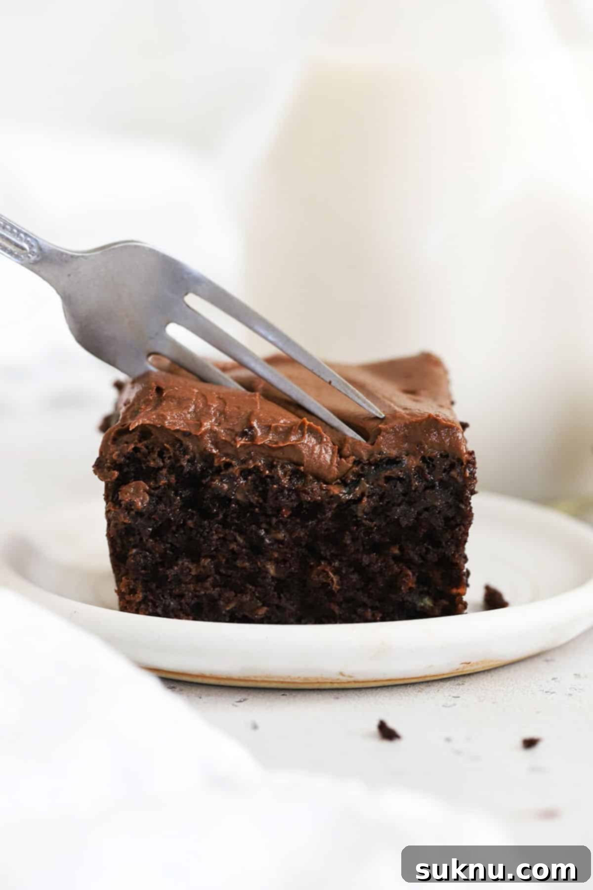 A fork cutting into a slice of gluten-free chocolate zucchini cake with rich chocolate frosting, showcasing its moist texture.