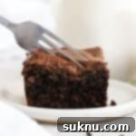a fork cutting into a slice of gluten-free chocolate zucchini cake with chocolate frosting