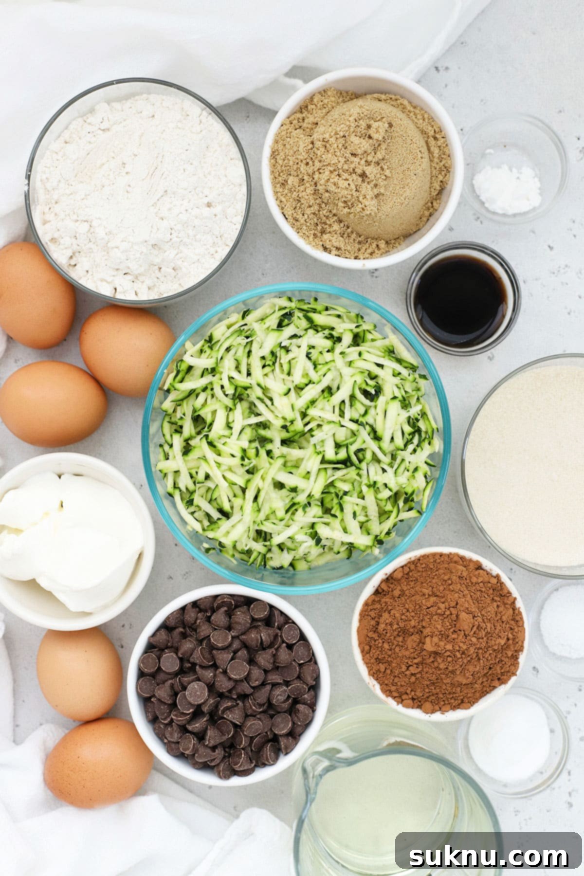 A collection of ingredients for gluten-free chocolate zucchini cake, neatly arranged on a white surface.