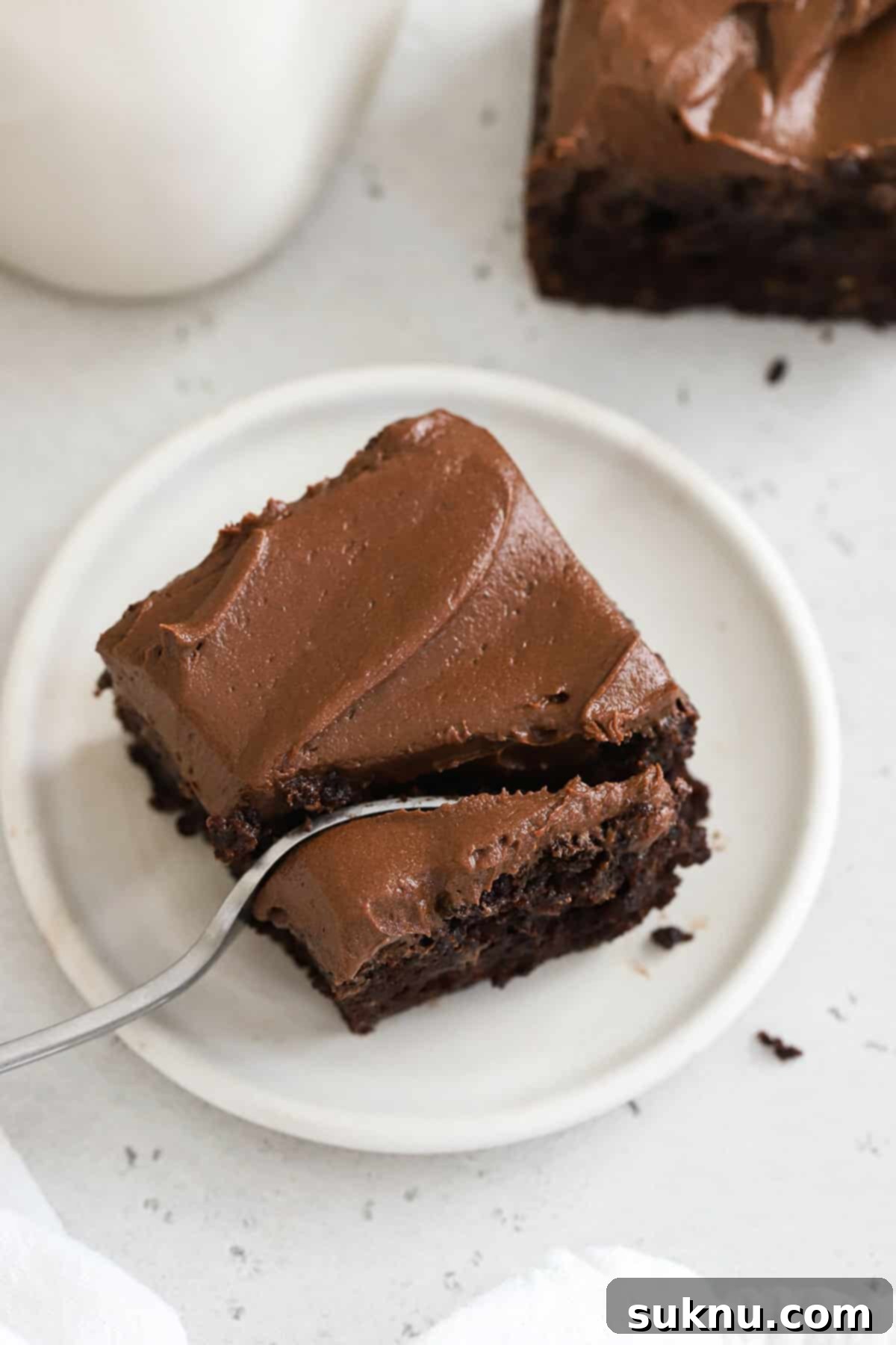 A fork taking a bite from a slice of moist gluten-free chocolate zucchini cake with creamy chocolate frosting.