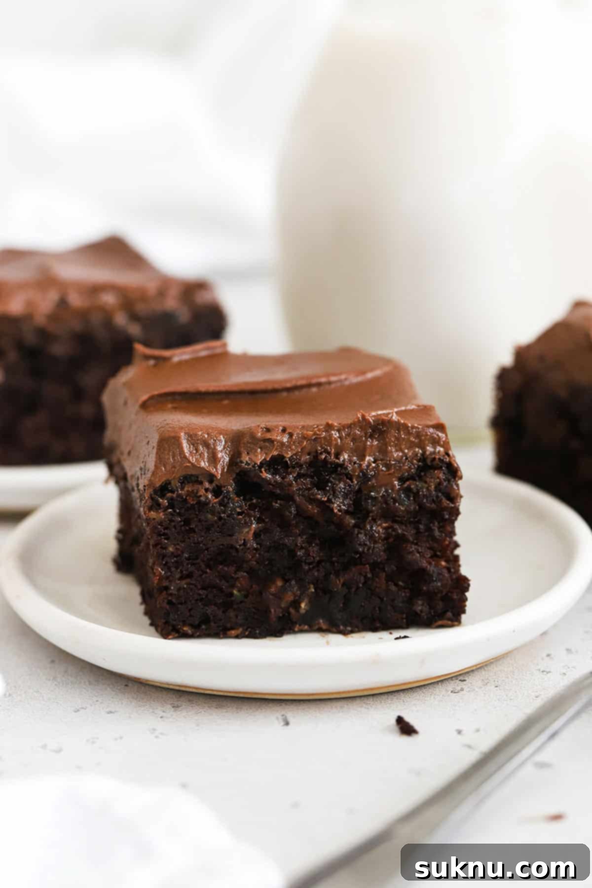 Slices of gluten-free chocolate zucchini cake with chocolate frosting on white plates, ready to be enjoyed.
