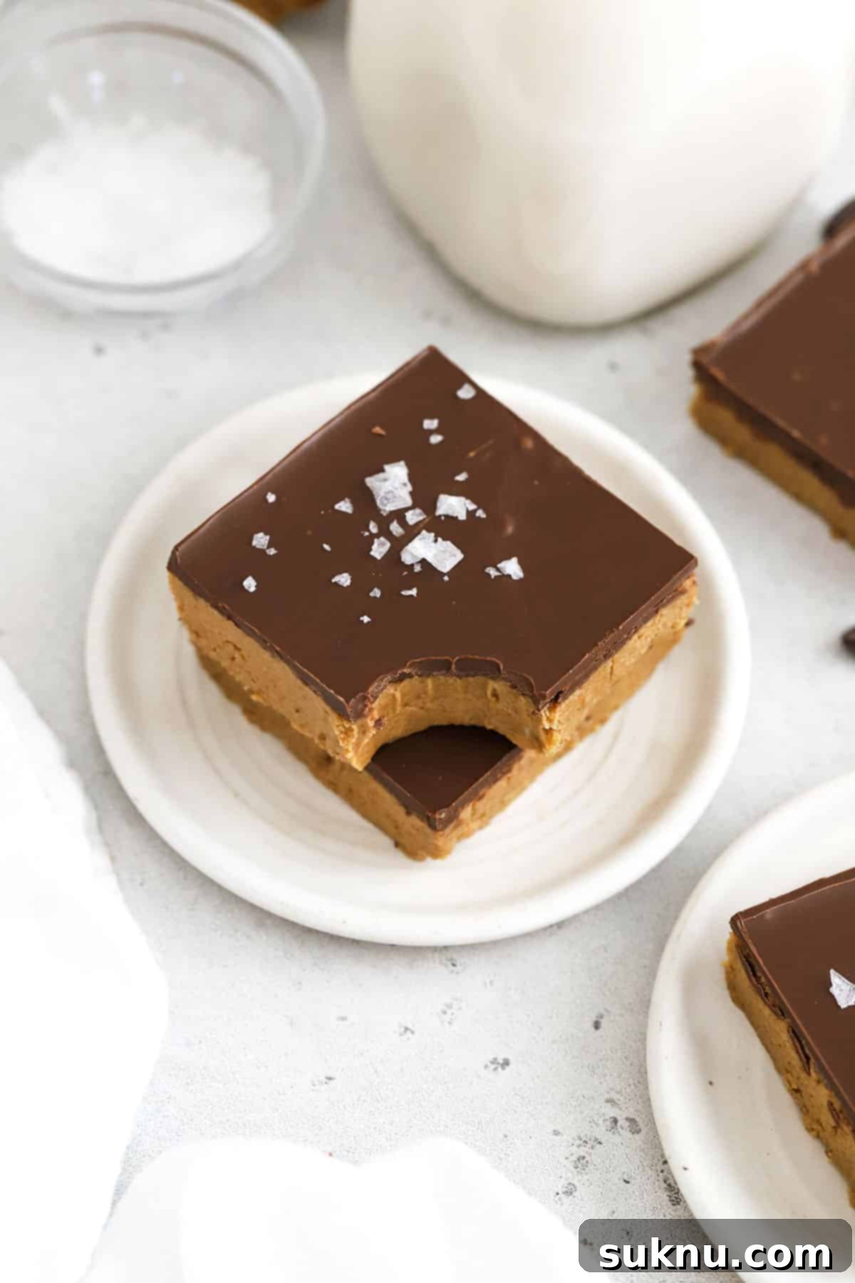 Gluten-free chocolate peanut butter bars stacked on a white plate, showcasing their rich layers and smooth topping
