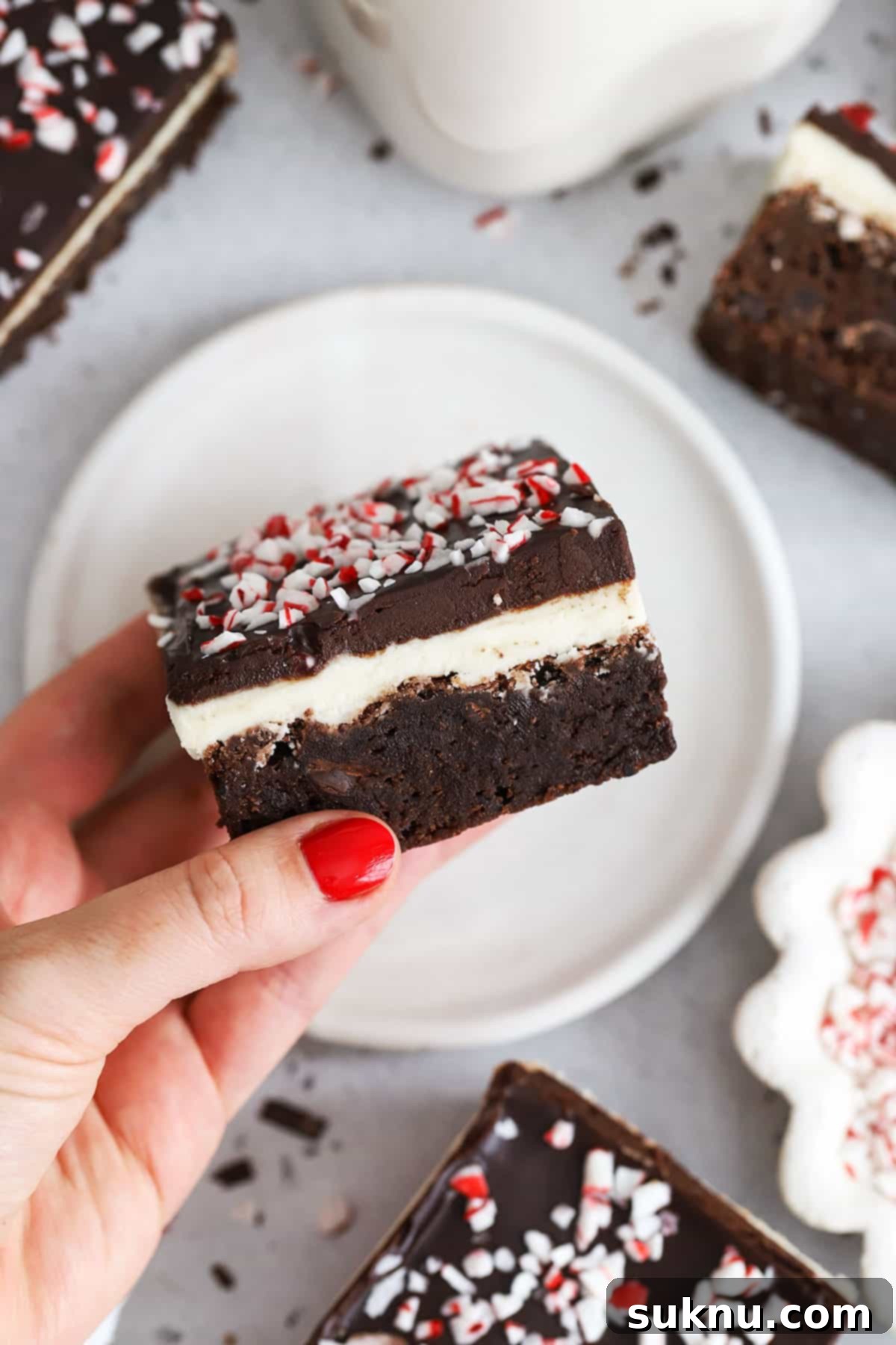 Festive Gluten-Free Peppermint Crunch Brownies 3 hand holding a multi-layered gluten-free peppermint brownie with frosting and ganache