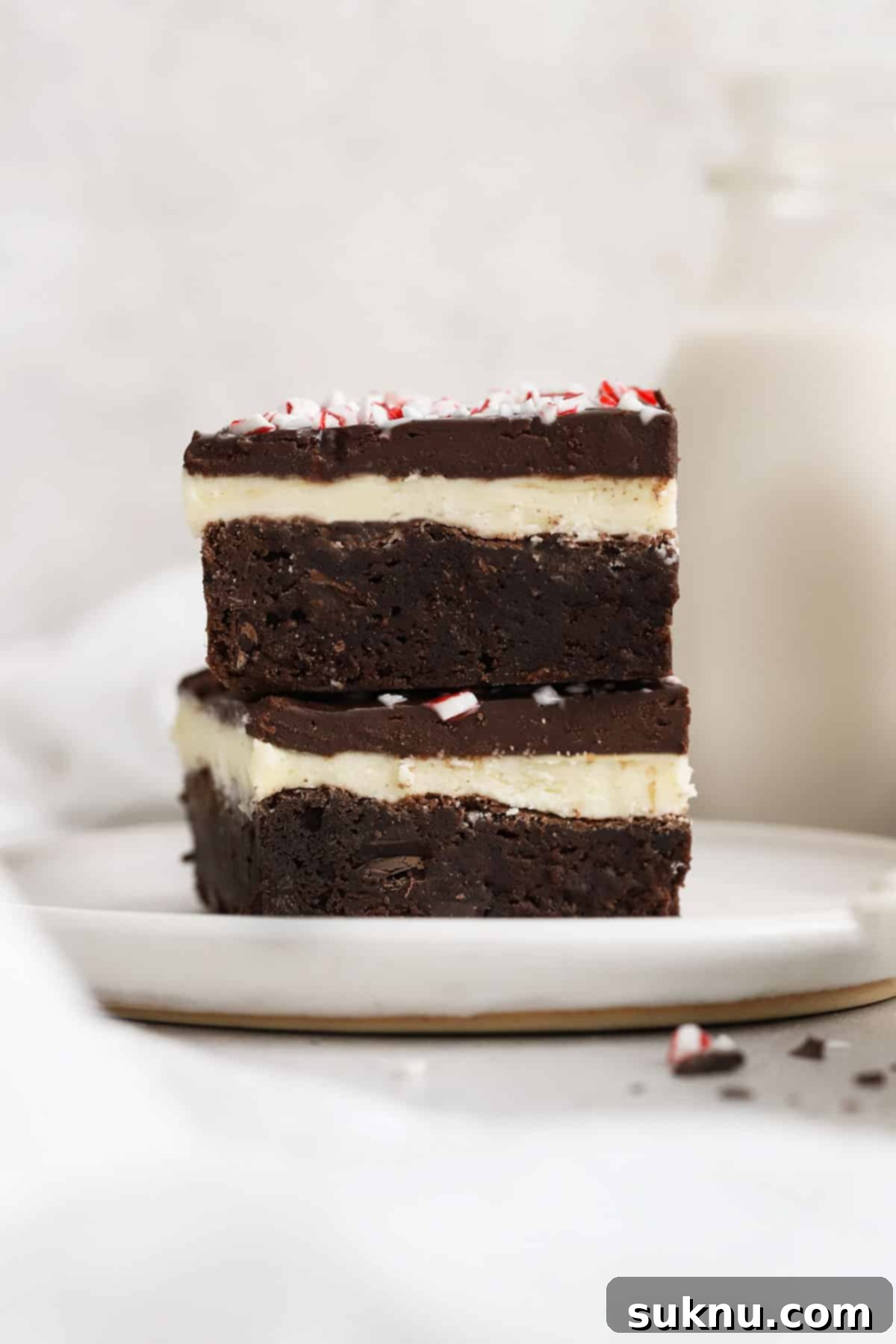 Festive Gluten-Free Peppermint Crunch Brownies 6 two gluten-free peppermint brownies with candy cane stacked on a white plate, showcasing layers