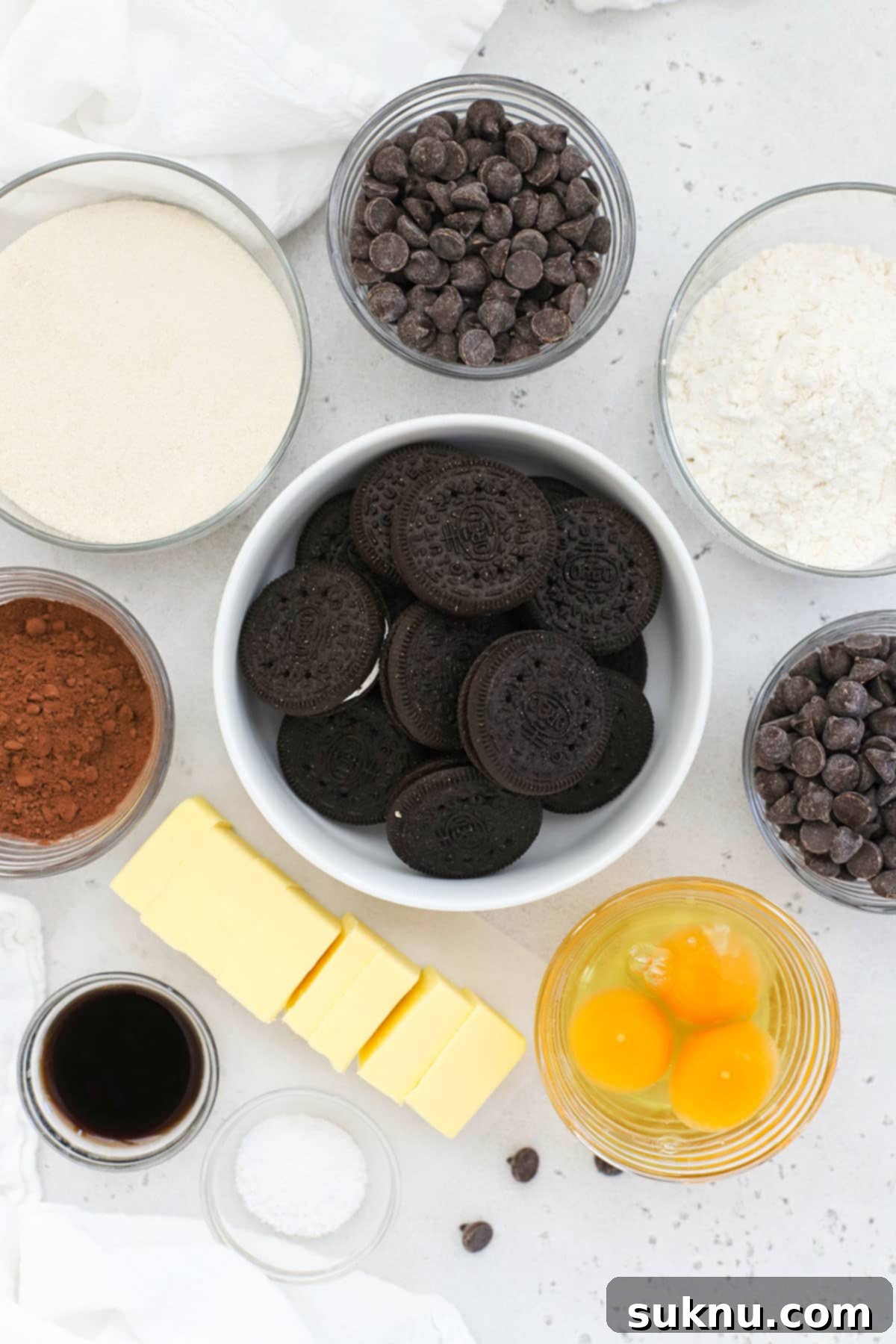 Array of ingredients laid out for making gluten-free Oreo brownies, including butter, chocolate chips, sugar, eggs, vanilla, flour, cocoa, salt, and gluten-free Oreos.