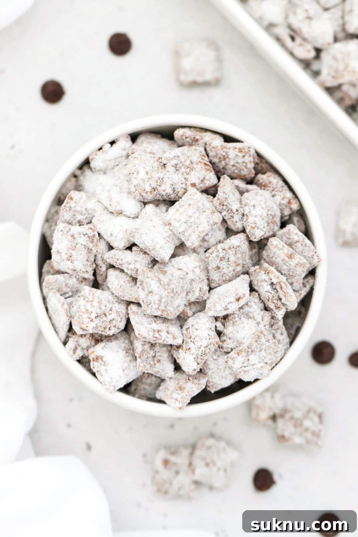 A white bowl overflowing with perfectly coated gluten-free muddy buddies, dusted with powdered sugar, ready to be enjoyed.