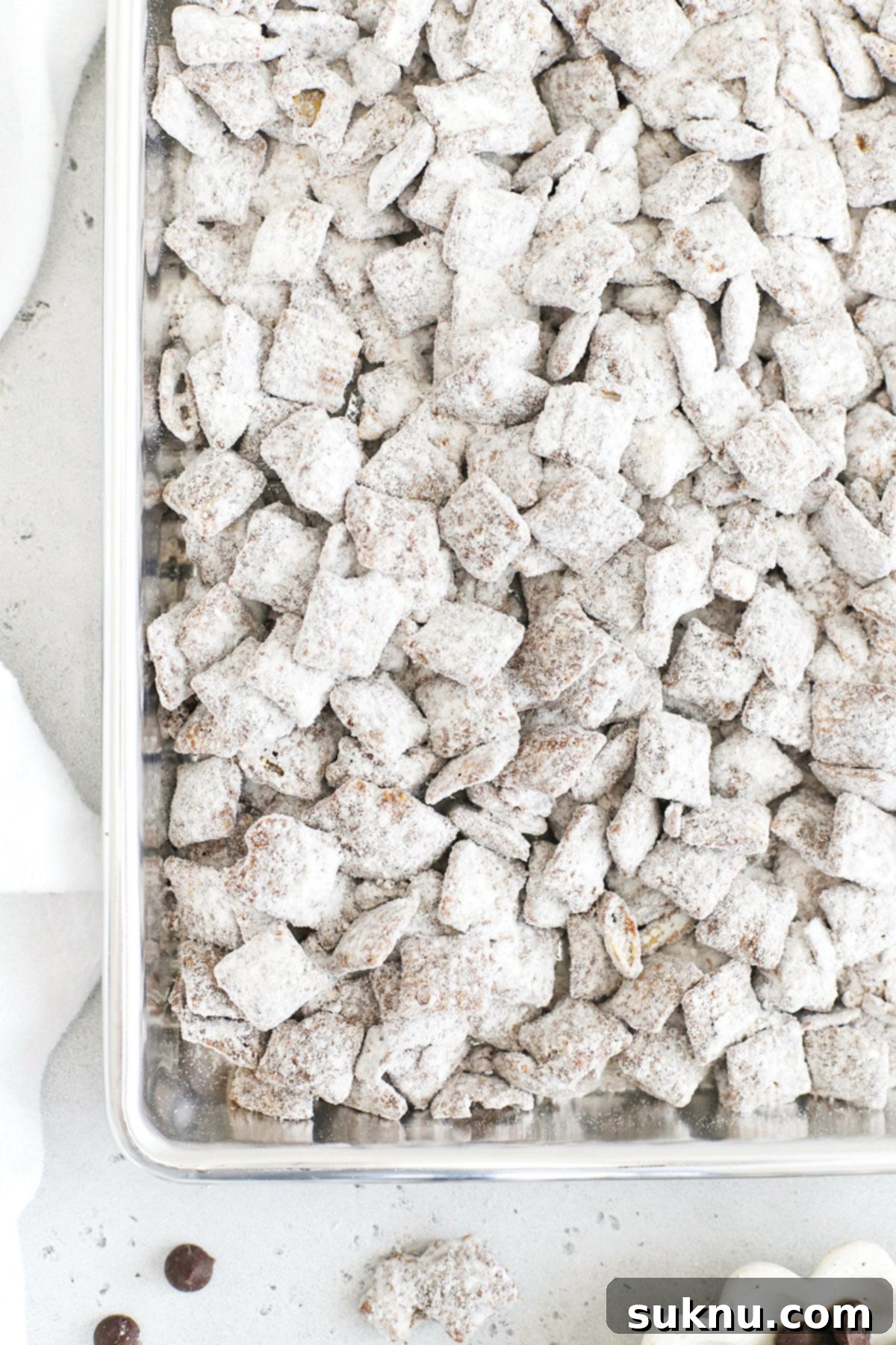 Gluten-free muddy buddies spread out on a parchment-lined baking sheet, showing the perfect powdered sugar coating.