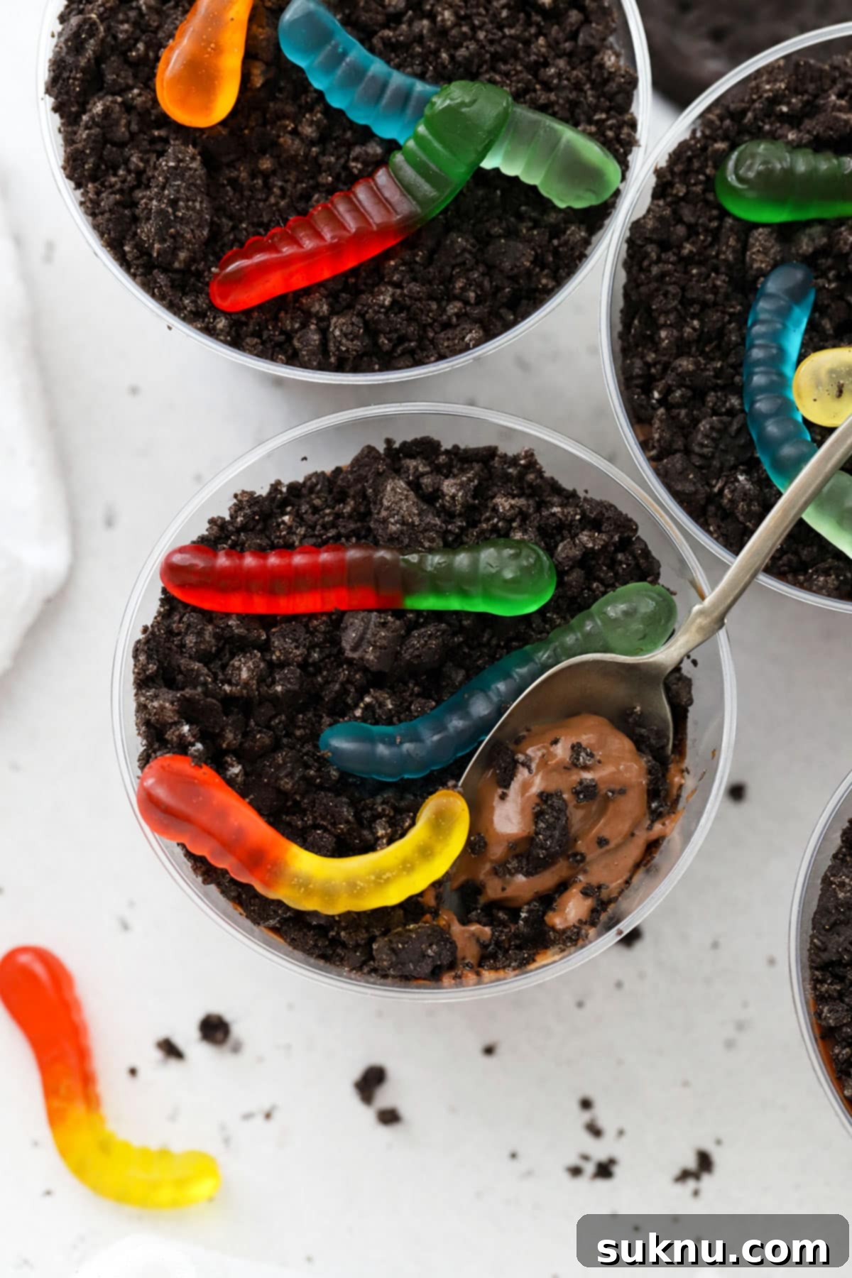 A closer look at a gluten-free dirt pudding cup, revealing distinct layers of homemade chocolate pudding and crushed gluten-free Oreo cookies, crowned with a bright gummy worm.