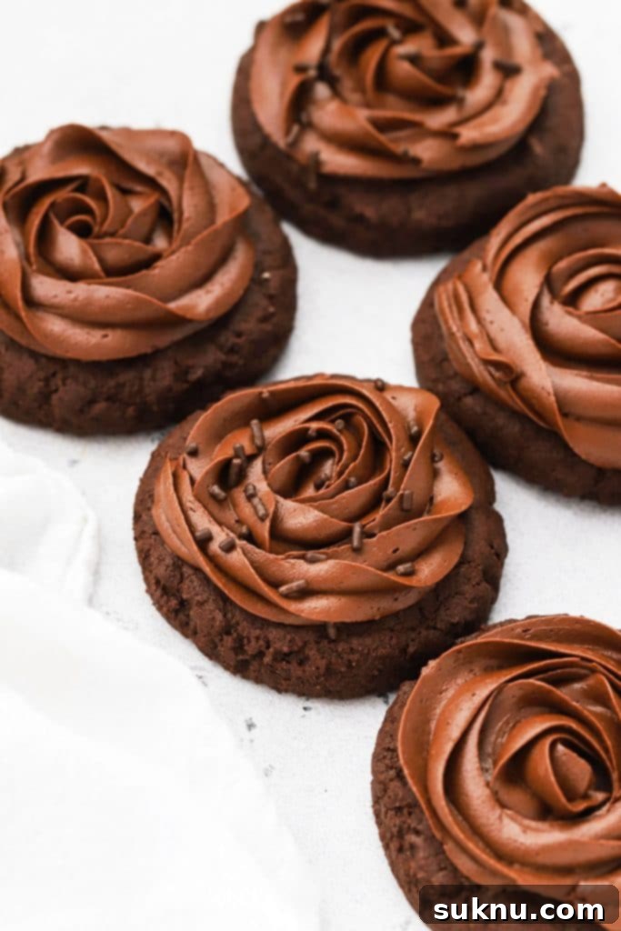 Decadent Gluten-Free Chocolate Buttercream 11 Front view of gluten-free crumbl chocolate cake cookies with chocolate frosting. One cookie has a bite taken out of it revealing the soft cakey center.