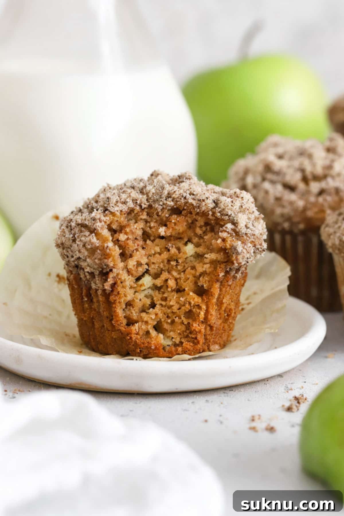 A close-up of a gluten-free apple muffin with a bite taken out, revealing its moist and fluffy interior.