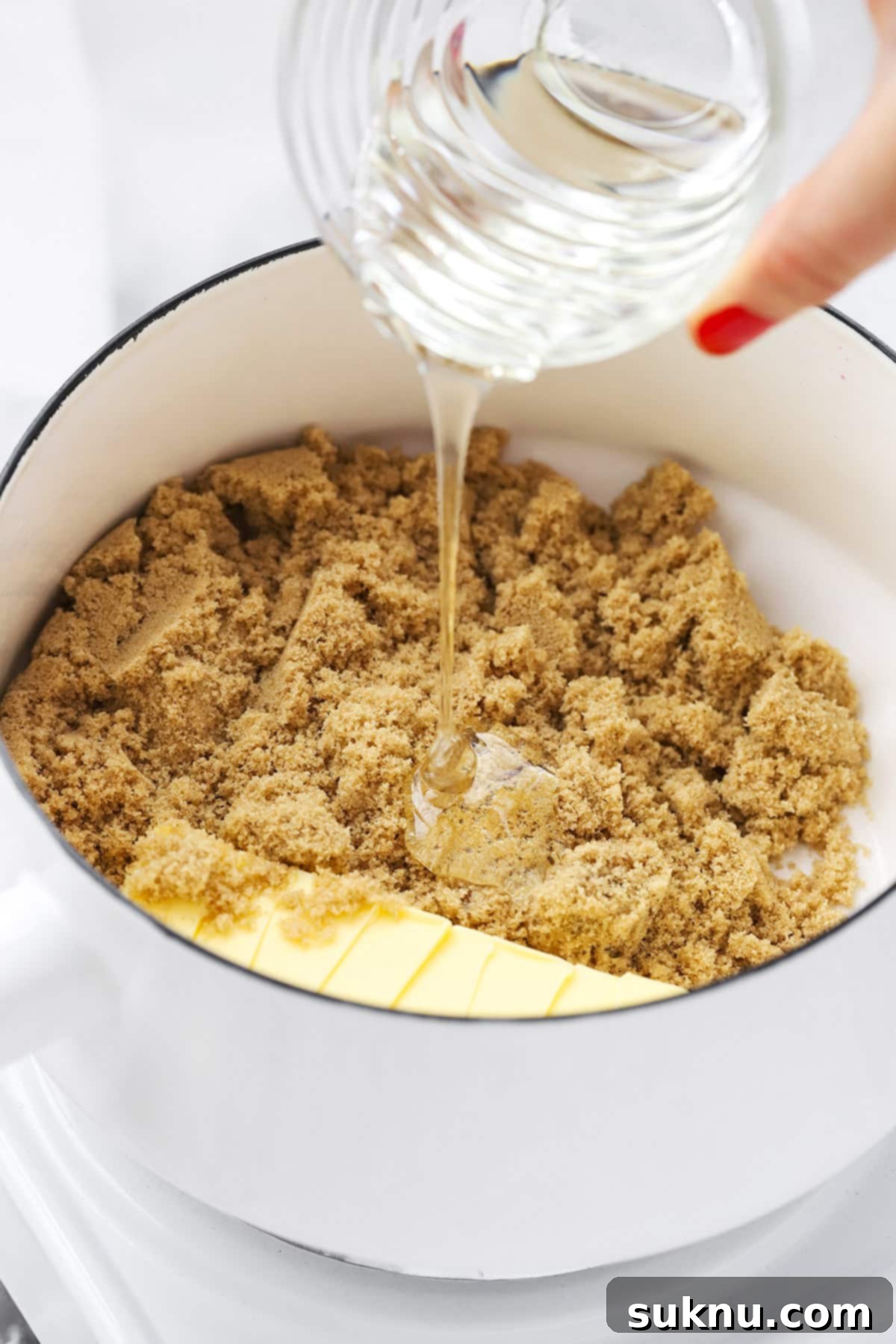 A close-up shot of corn syrup being poured into a saucepan with brown sugar and butter, illustrating the process of making caramel sauce for homemade caramel corn.
