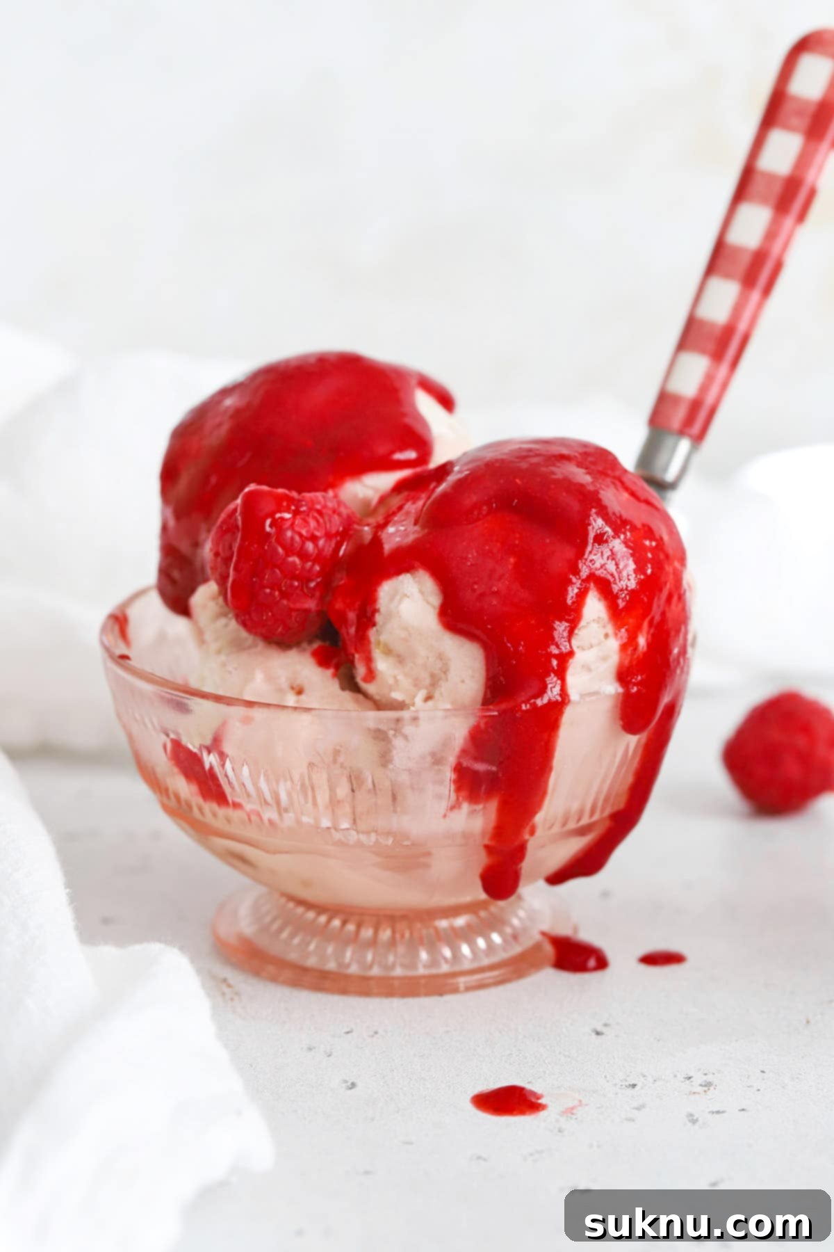 A vibrant close-up of strawberry ice cream lavishly covered with a glossy, red raspberry sauce, creating a tantalizing dessert image.