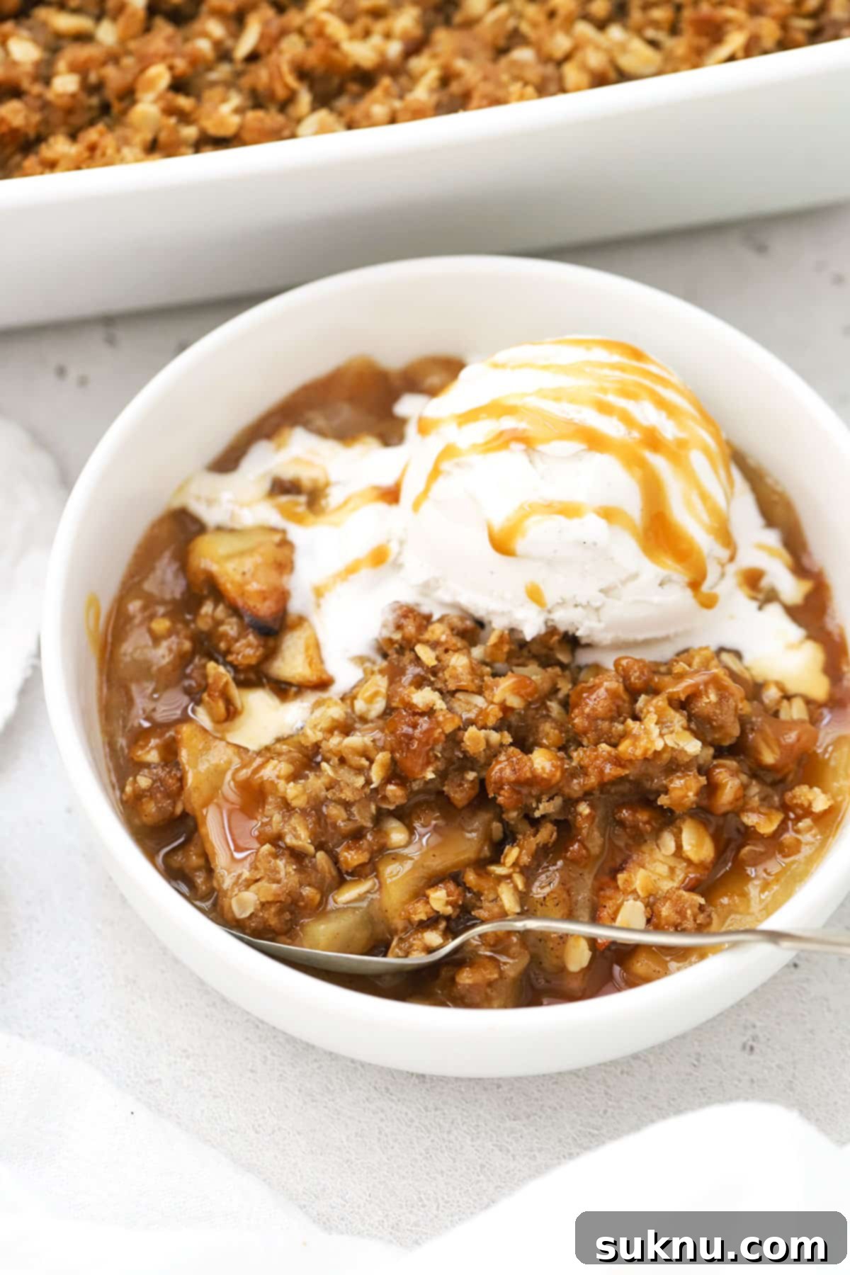 Decadent Gluten-Free Caramel Apple Crisp 7 A bowl of gluten-free apple crisp with caramel sauce and a scoop of ice cream, viewed from above.