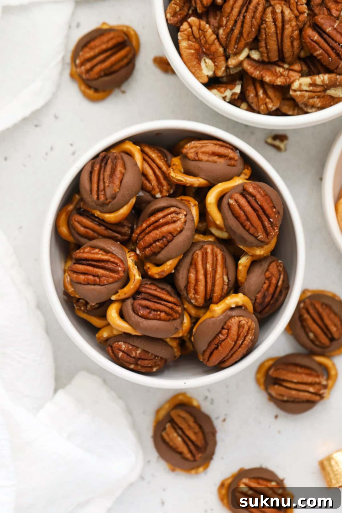 Gluten-Free Rolo Pretzel Turtles 4 A pristine white bowl showcasing an assortment of gluten-free Rolo pretzel turtles, each topped with a pecan.