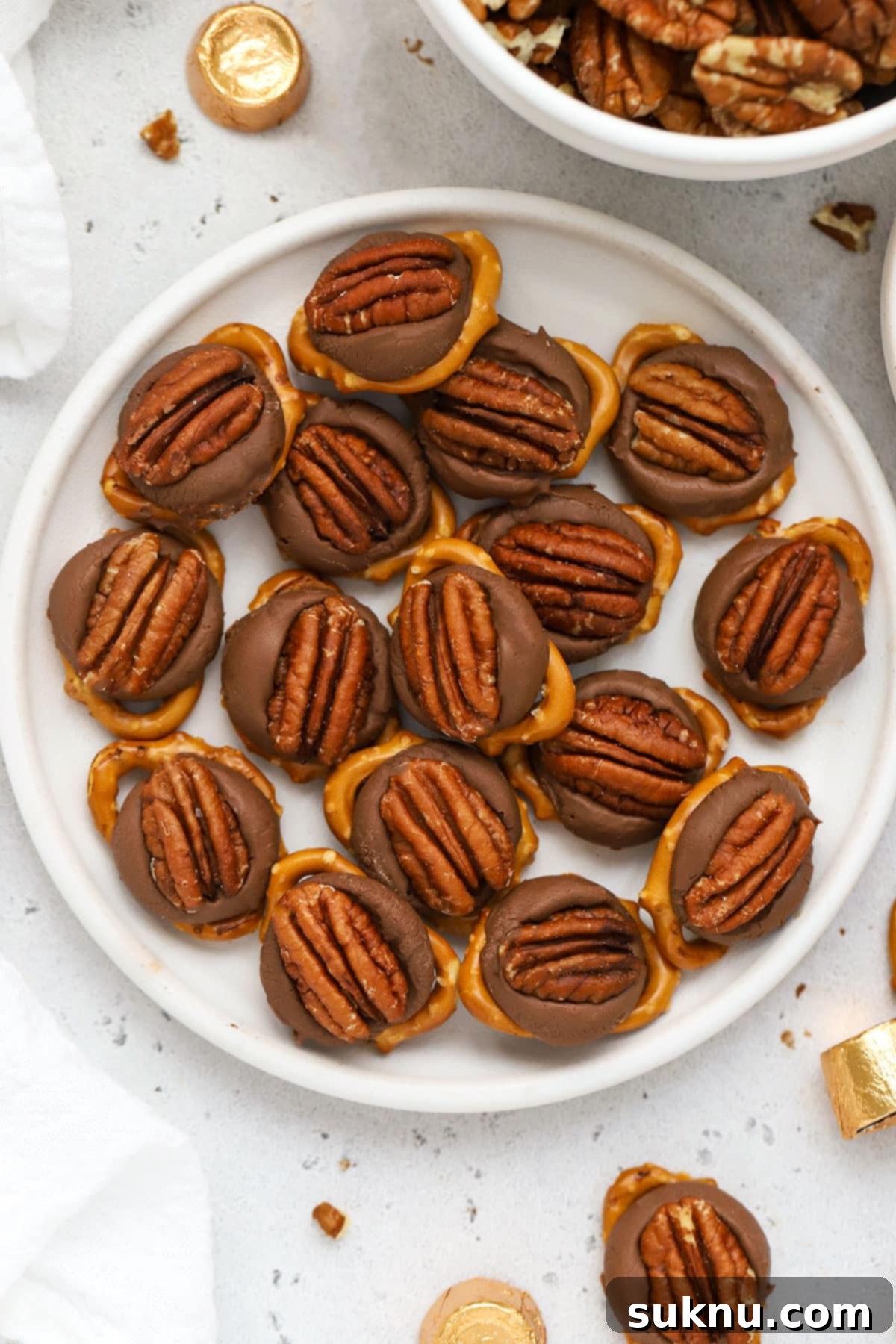 Gluten-Free Rolo Pretzel Turtles 8 A close-up shot of gluten-free Rolo turtles on a white plate, showcasing two distinct topping styles: M&M's and pecans.