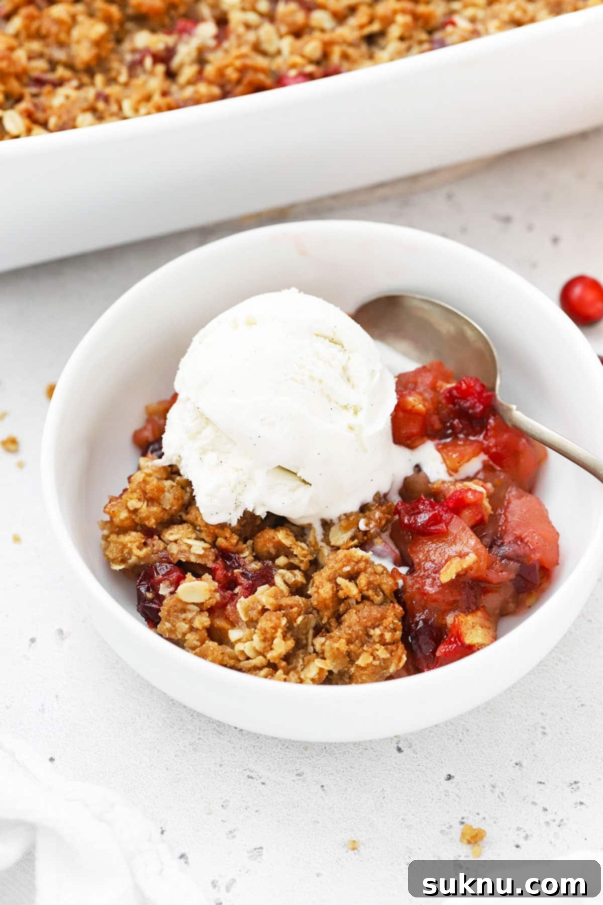 gluten-free apple cranberry crisp in a white bowl with a scoop of vanilla ice cream
