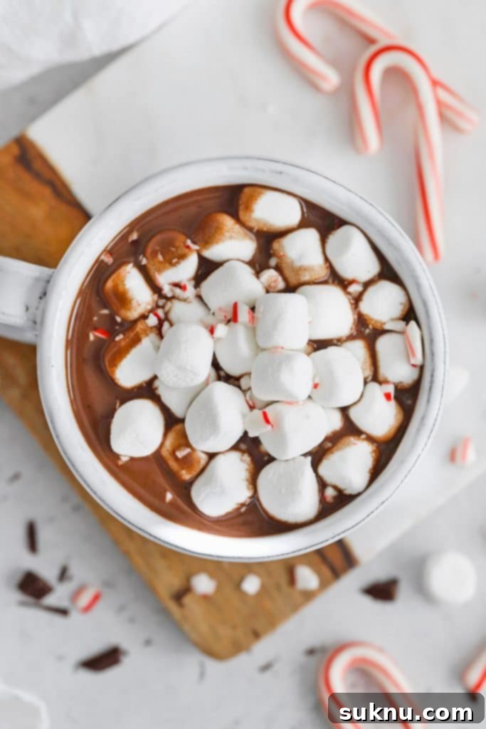 Overhead view of a steaming mug of vegan peppermint hot chocolate topped with marshmallows from Sweets & Thank You