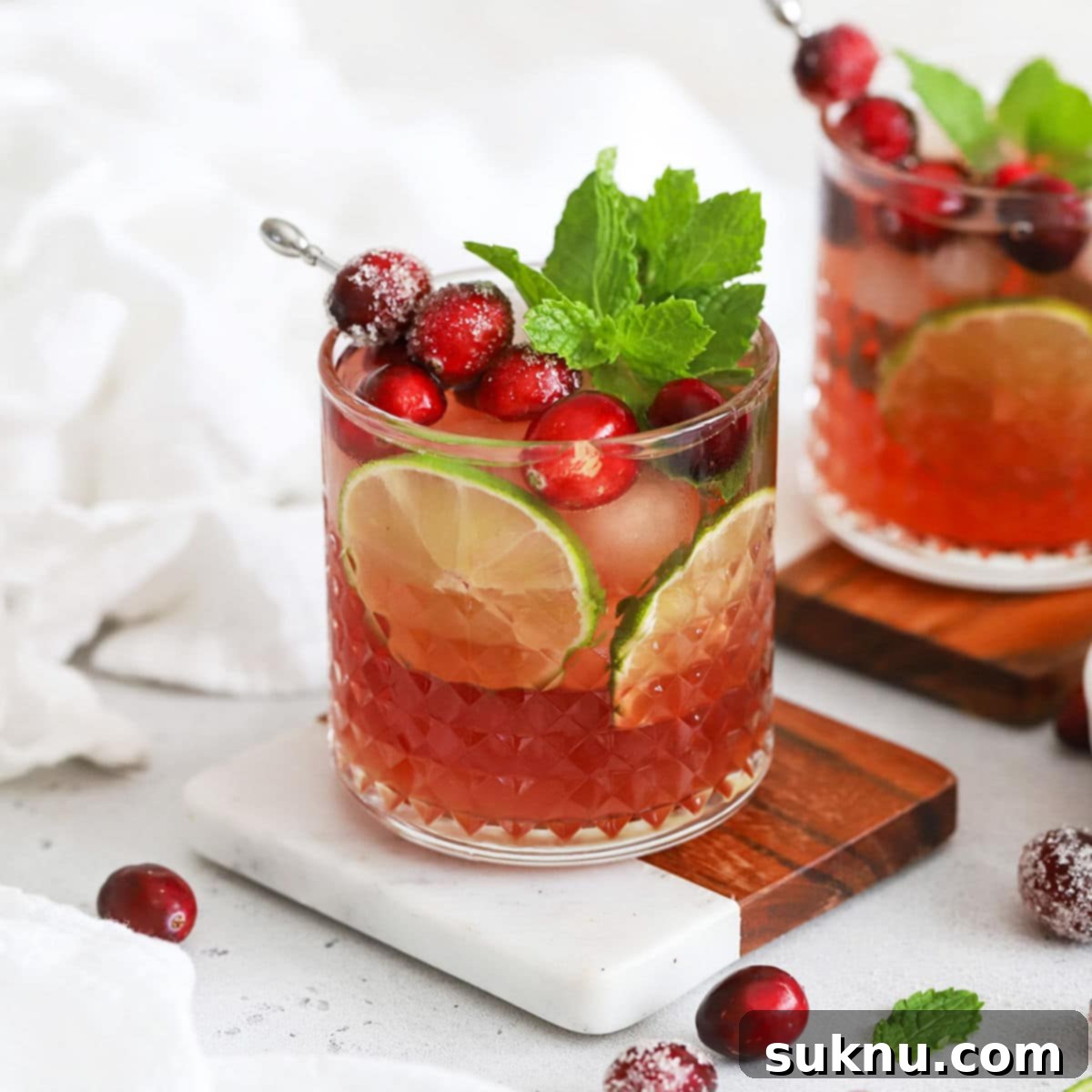 two cranberry lime mocktails in rocks glasses garnished with sugared cranberries and fresh mint
