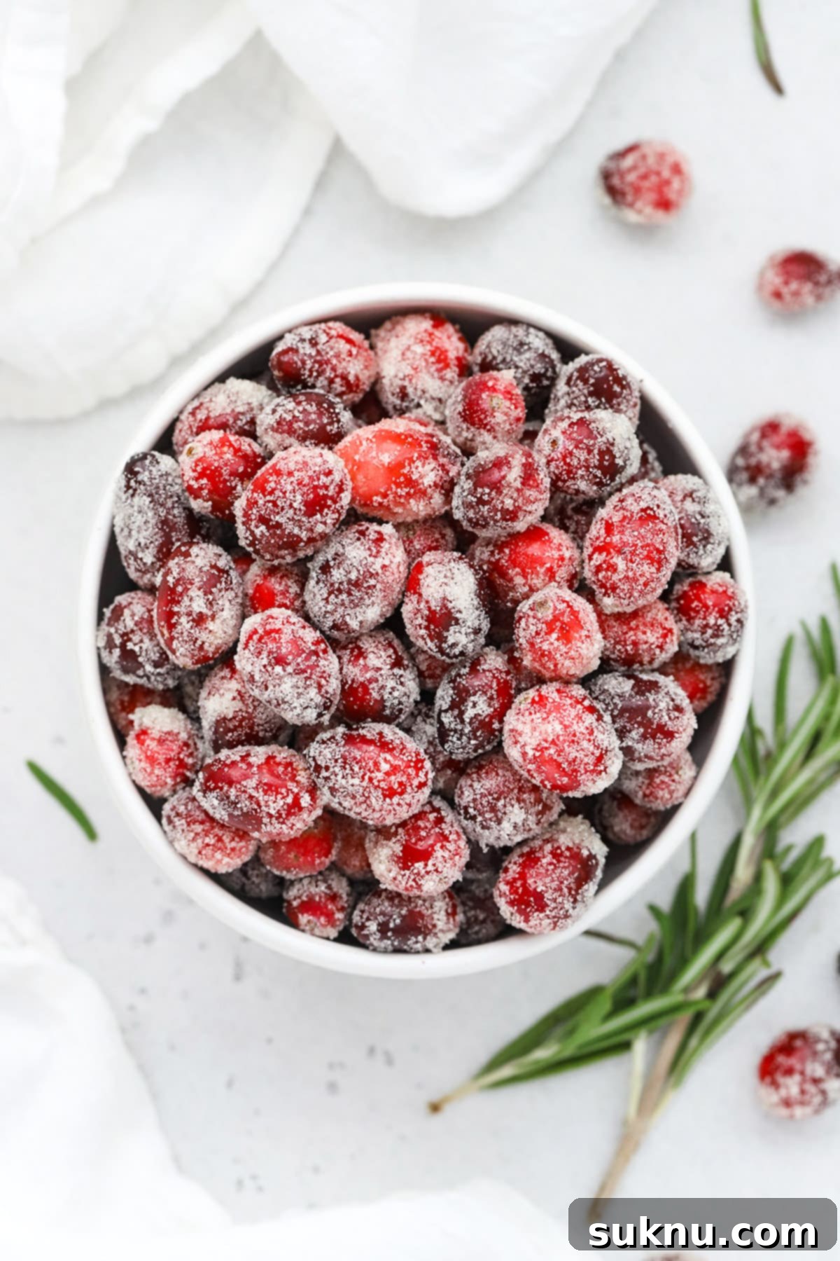 Overhead view of a bowl of sugared cranberries with a sprig of rosemary in the background
