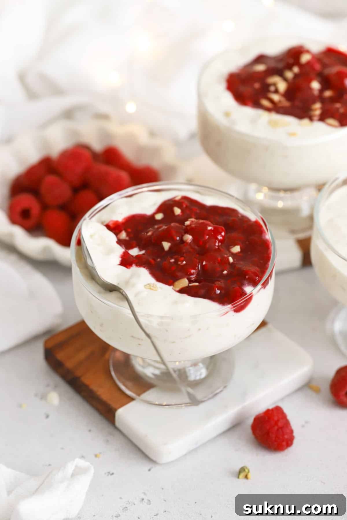 Elegant dessert bowls filled with creamy Risalamande, garnished with fresh raspberries and a swirl of raspberry sauce, perfect for a festive occasion.
