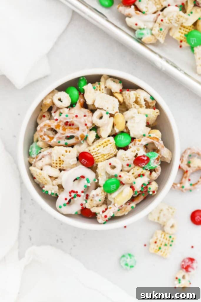 A white bowl of gluten-free Christmas Chex Mix with festive M&Ms and pretzels.