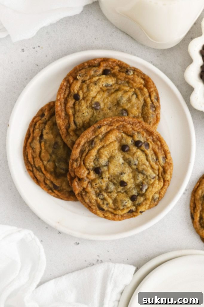 Three crisp gluten-free chocolate chip cookies on a white plate, perfect for a light snack.