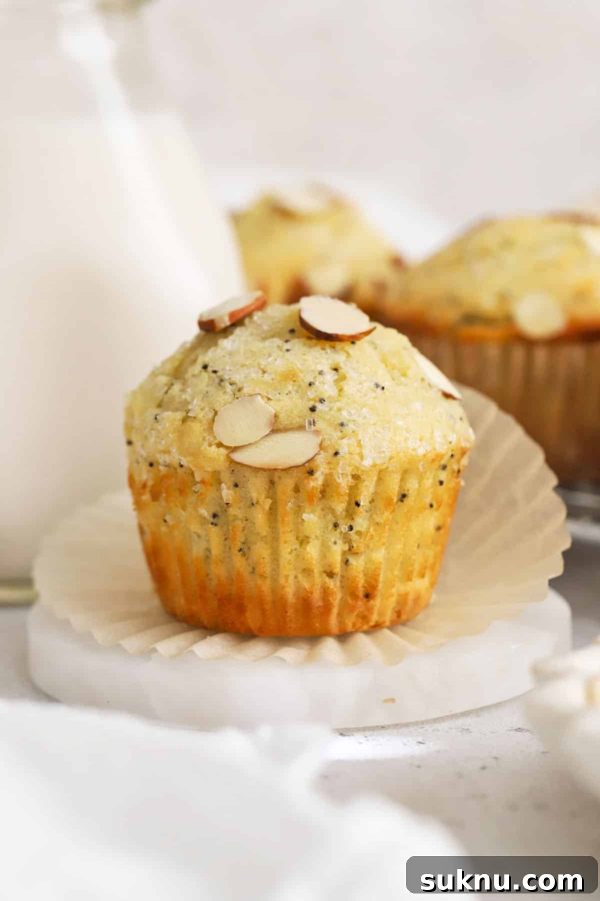 Close-up of golden brown gluten-free almond poppy seed muffins, topped with sparkling sugar and sliced almonds, invitingly soft and fluffy.