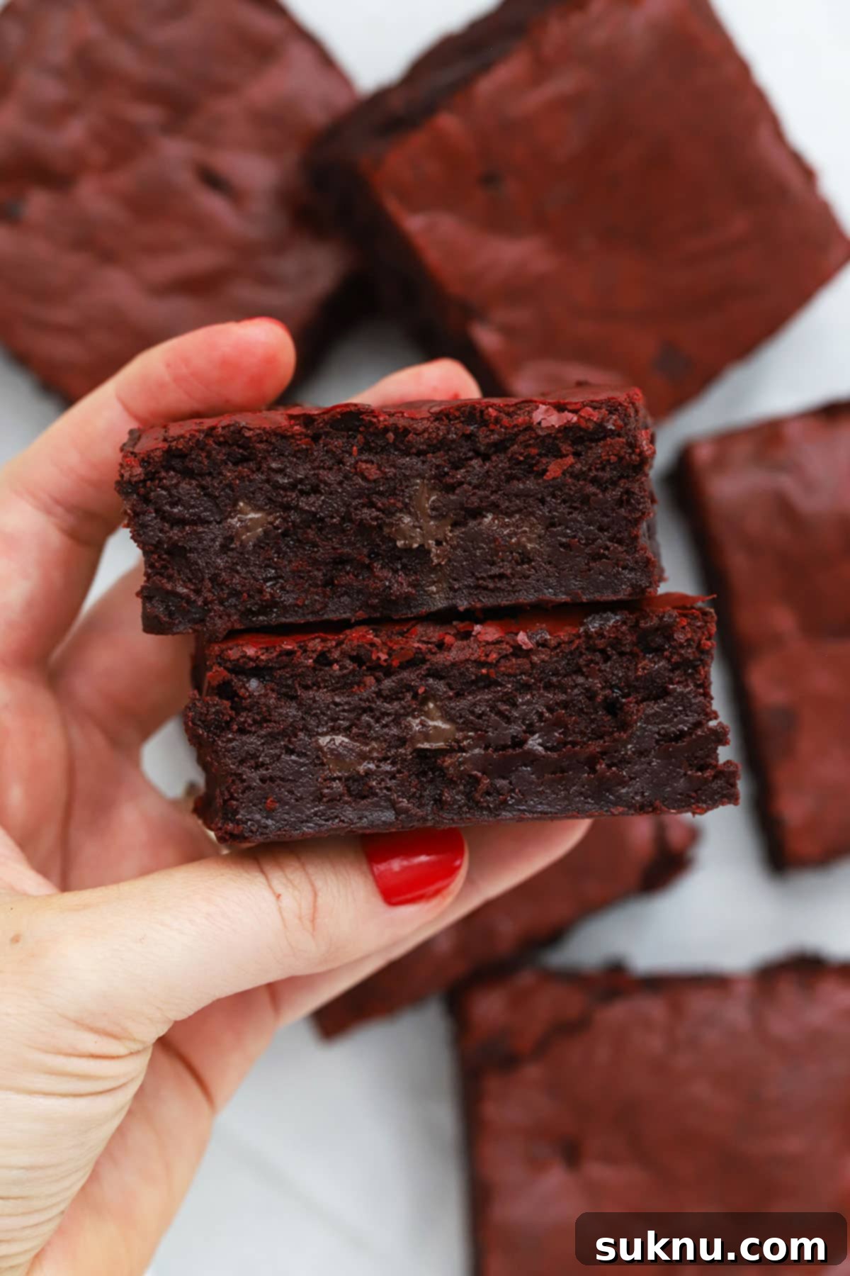 A hand holding two perfectly fudgy gluten-free red velvet brownies, showing their rich texture.
