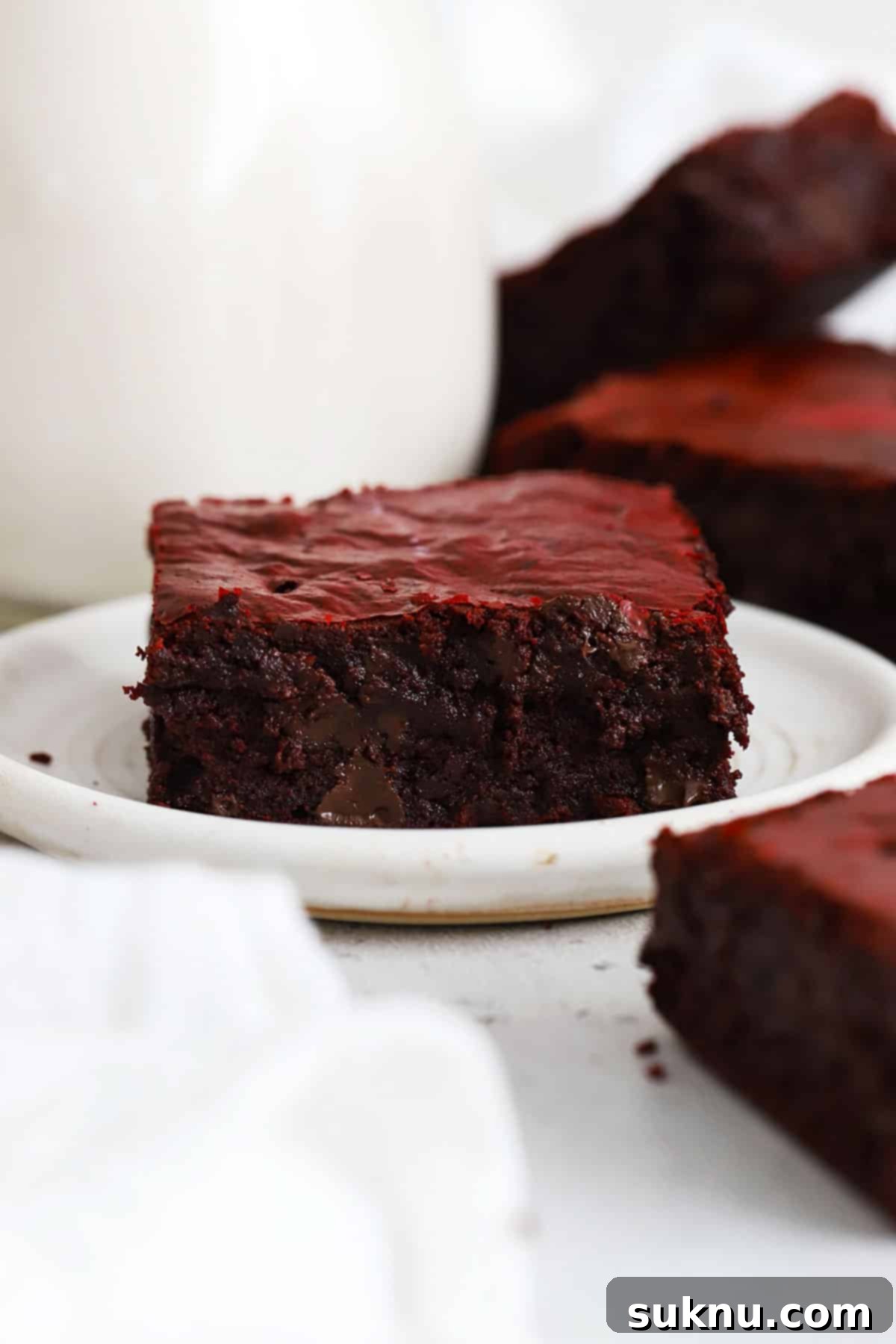 A close-up front view of a single gluten-free red velvet brownie on a white plate, highlighting its texture and color.