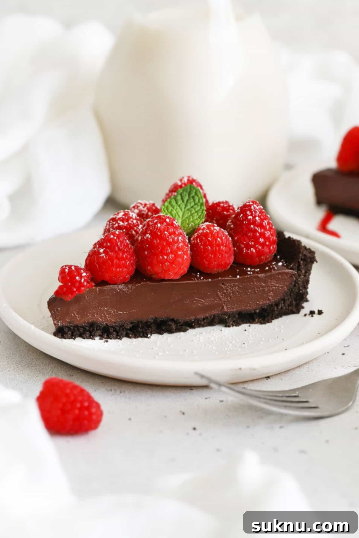 A perfectly sliced gluten-free chocolate ganache tart, elegantly presented on a white plate with fresh raspberries.