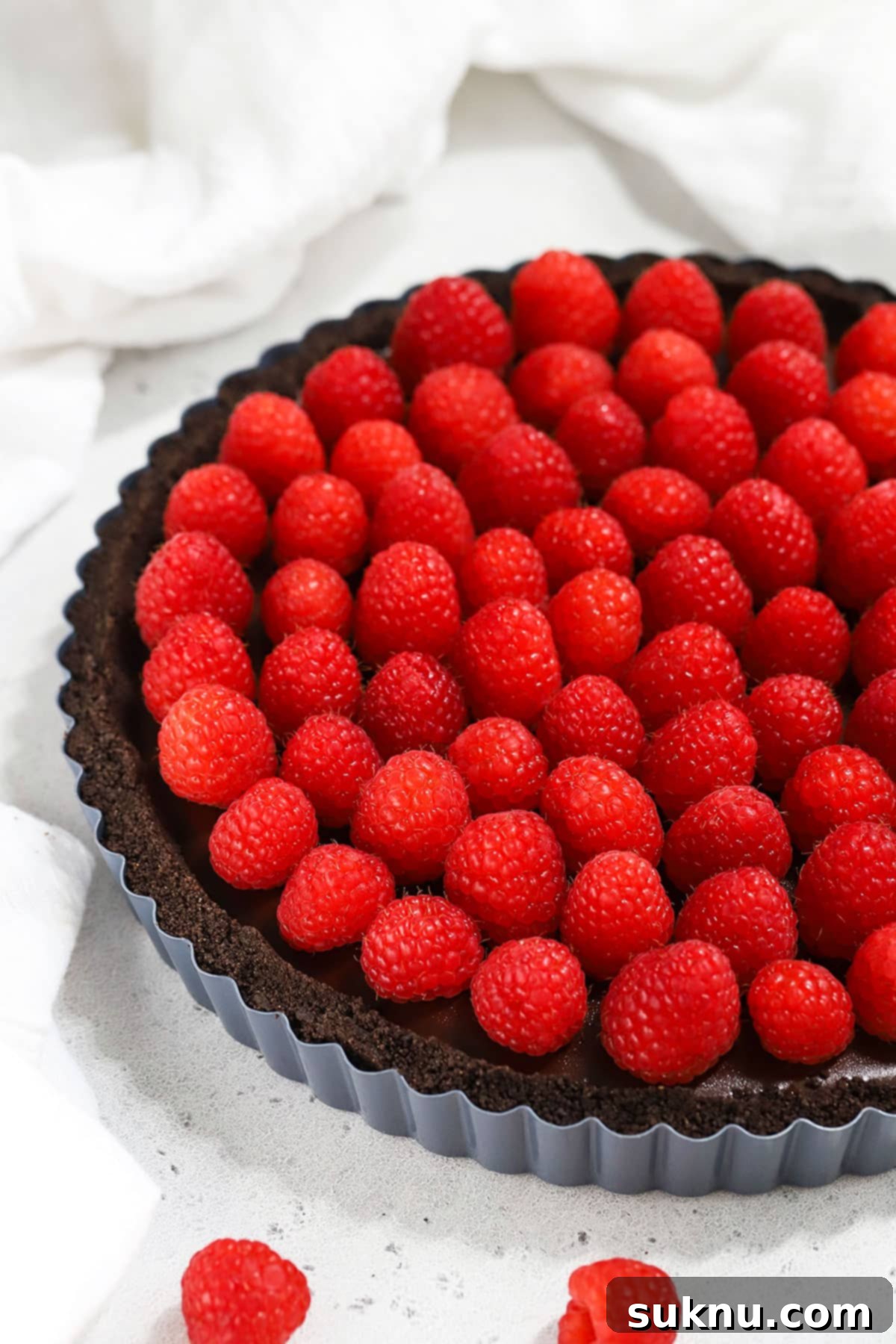 A freshly assembled gluten-free chocolate tart, beautifully topped with a vibrant layer of fresh raspberries, ready for serving.