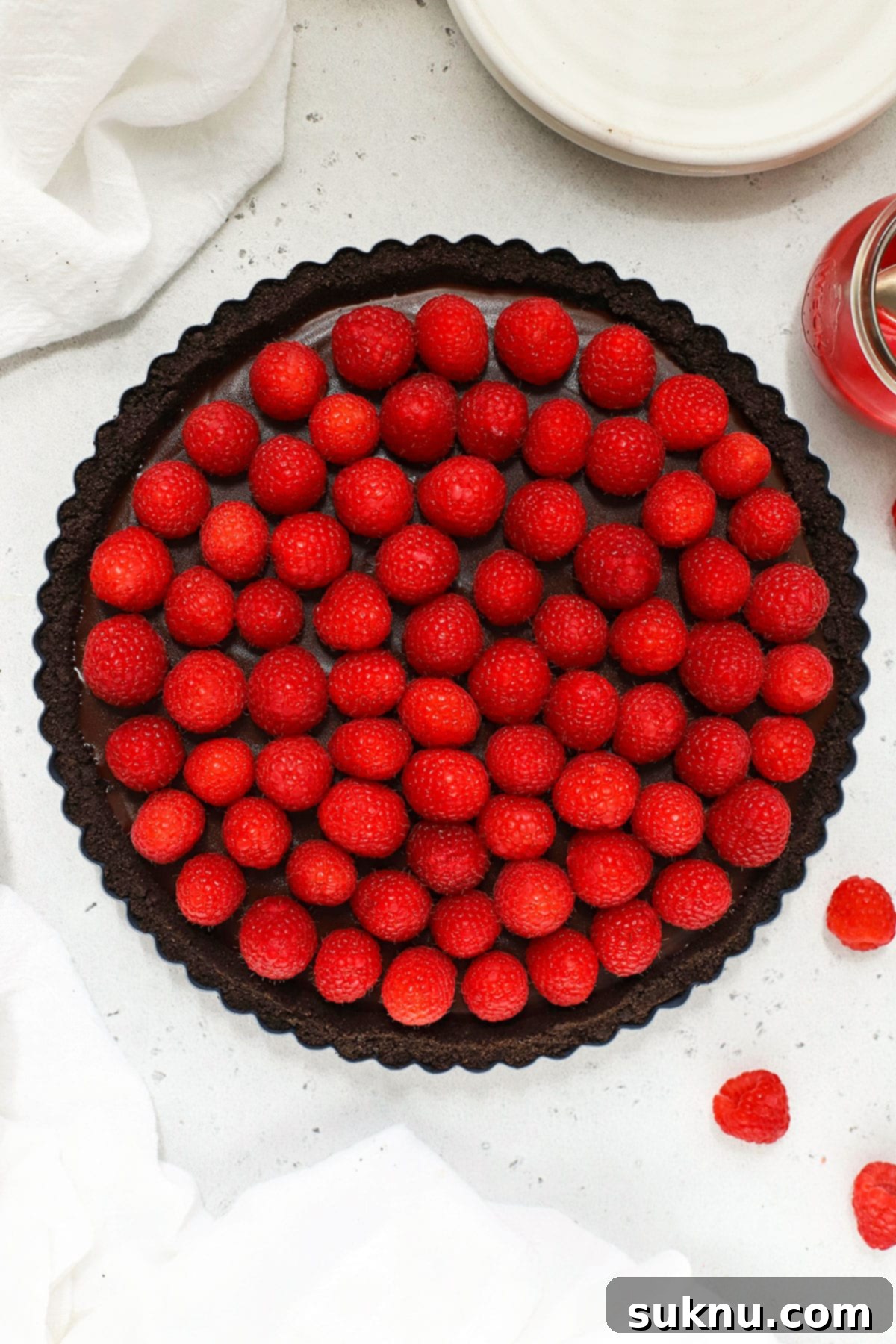 An elegantly plated slice of gluten-free chocolate tart, generously topped with fresh raspberries, showcasing its rich texture.