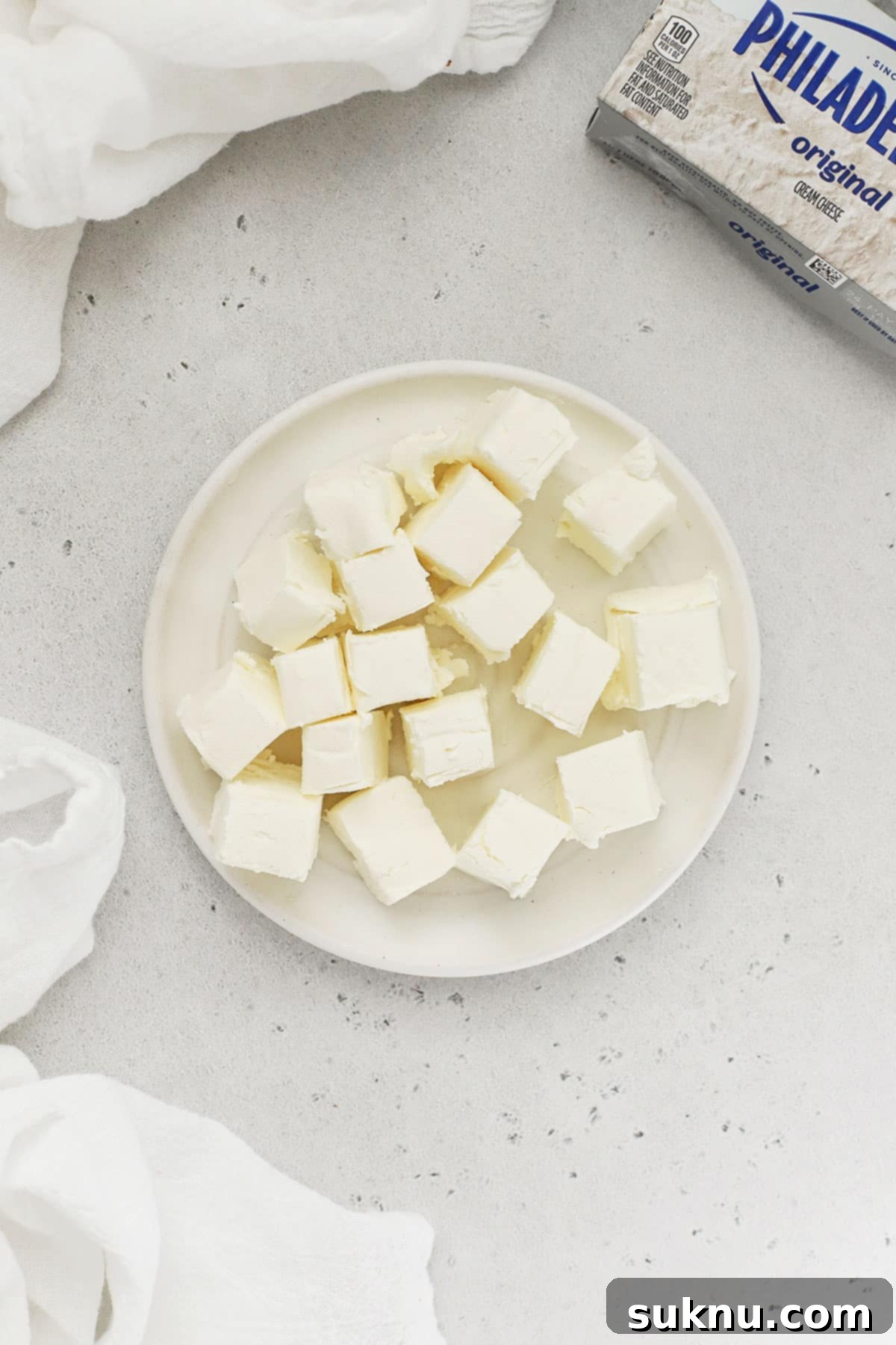 Soft Cream Cheese in Minutes 5 A block of cream cheese expertly cut into small 1/2-inch cubes on a white plate to accelerate softening