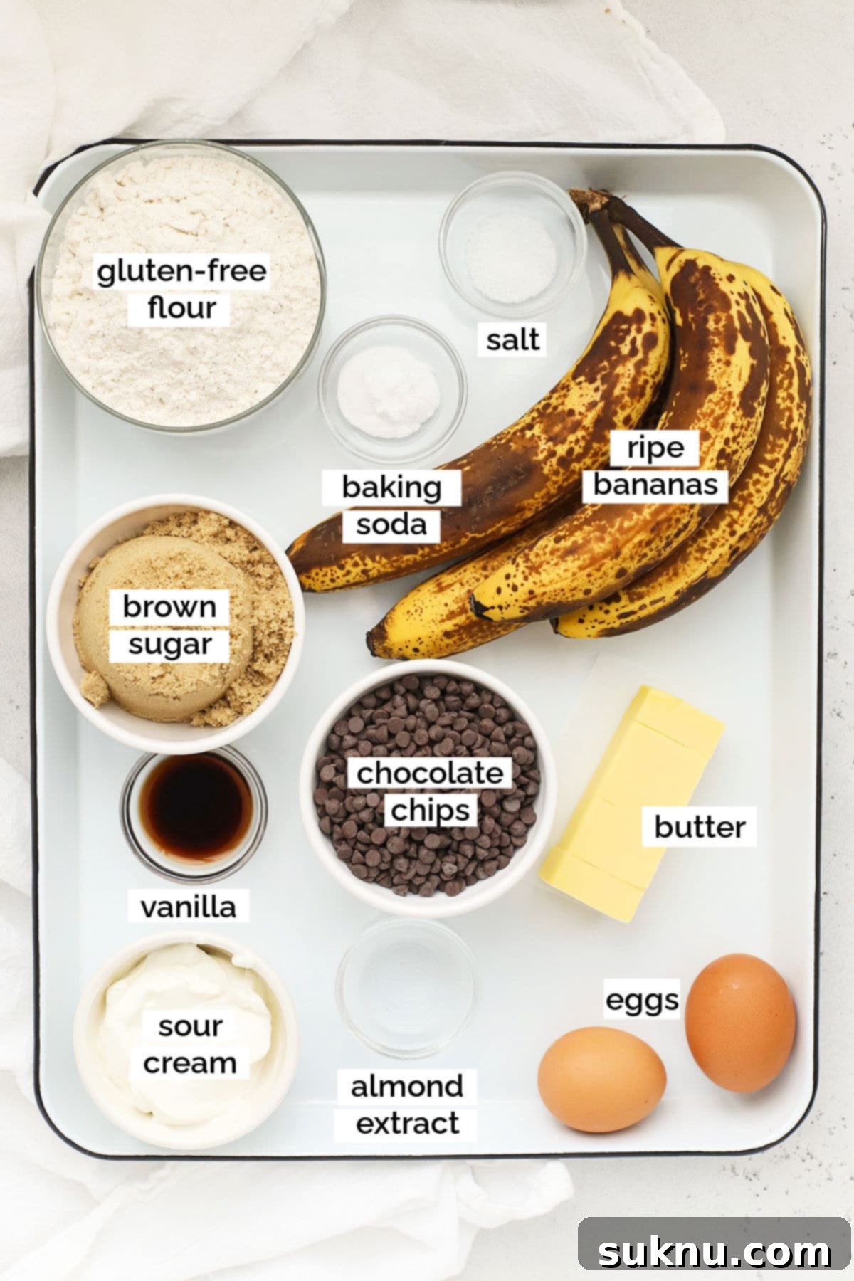 A collection of fresh ingredients laid out, including ripe bananas, chocolate chips, flour, and butter, ready for making gluten-free chocolate chip banana bread.