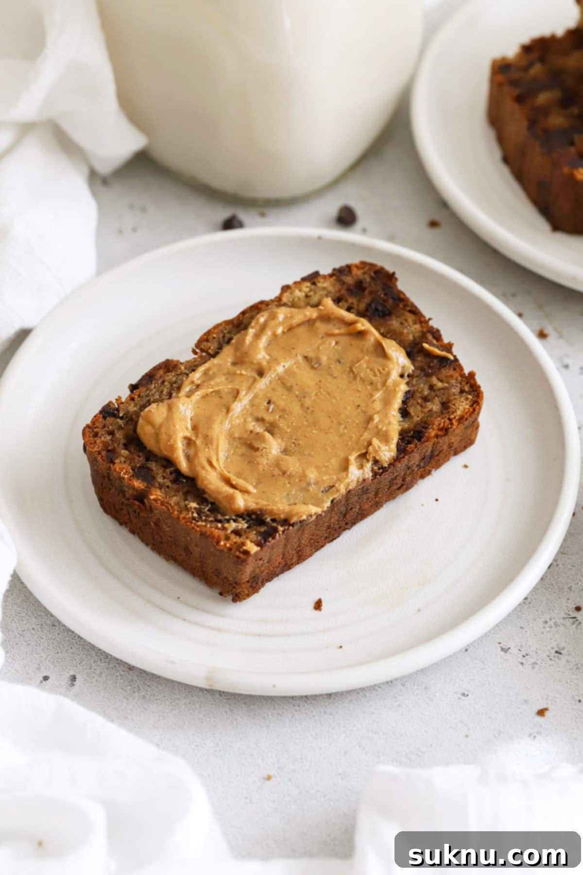 A slice of gluten-free chocolate chip banana bread generously spread with peanut butter, ready to be enjoyed.