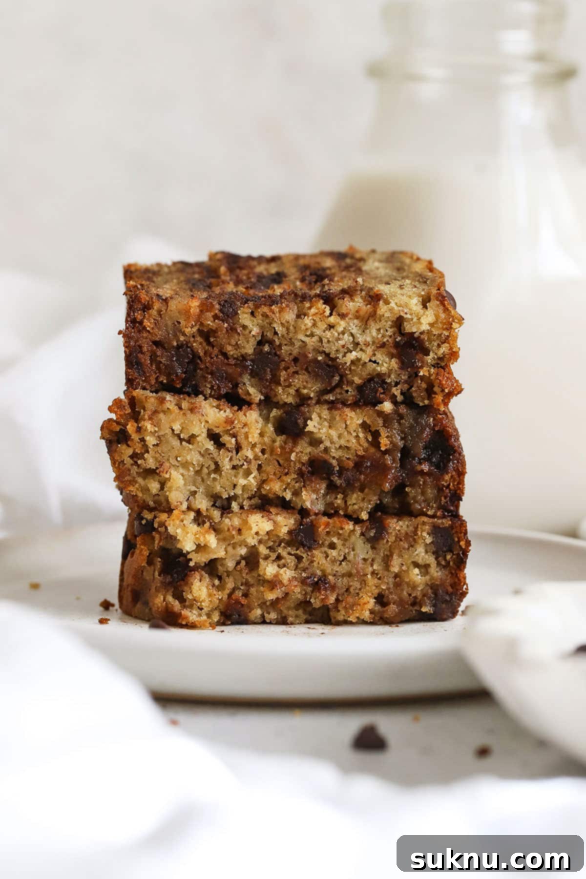 Three perfectly golden slices of gluten-free chocolate chip banana bread, stacked on a white plate, showcasing their soft, appealing texture.